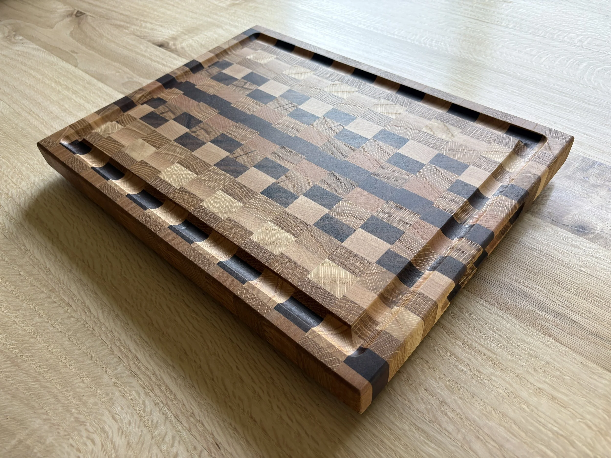 mixed hardwood cutting board with juice grooves on a hardwood table, white oak, red oak, black oak, maple, walnut