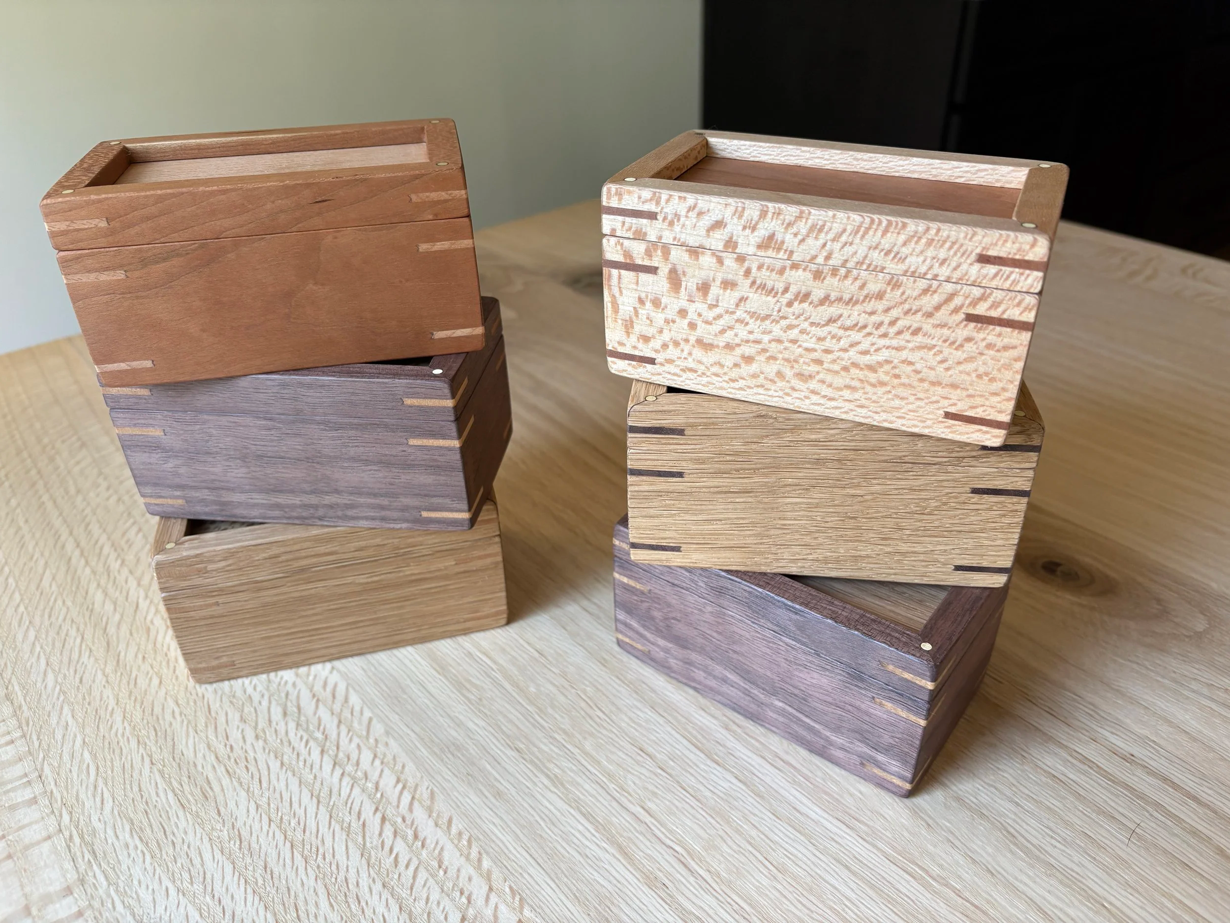 Six wooden boxes in various shades and wood grains stacked on a light wood surface.
