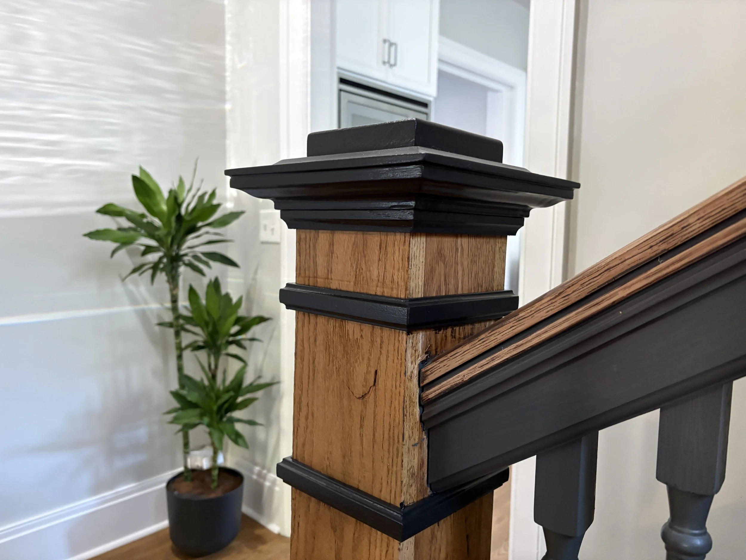black painted finial and trim on a newel post in a white room with hardwood floors