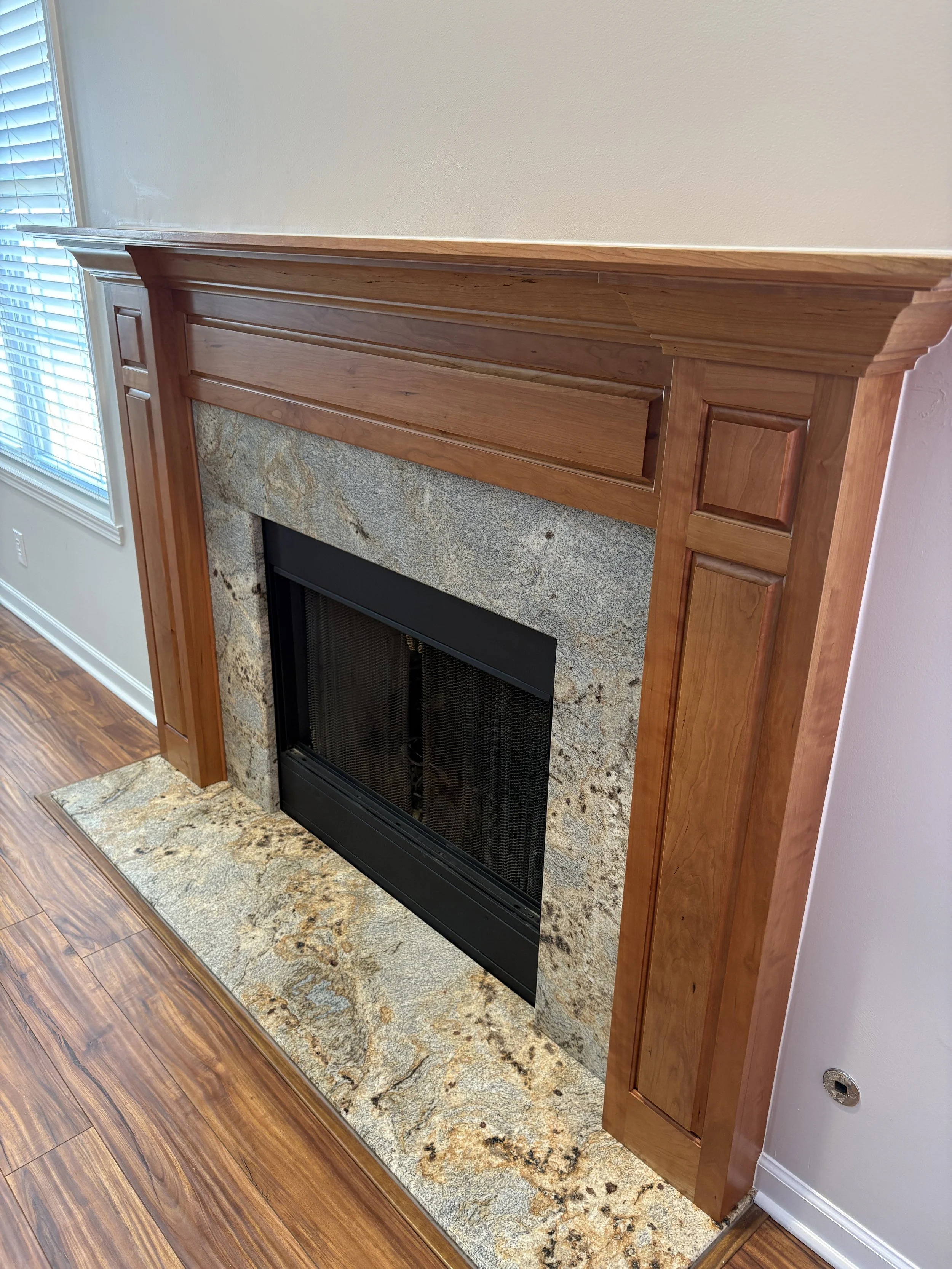 cherry wood fireplace mantel with raised panels in a beige room with stone hearth, wood floors, and white baseboard