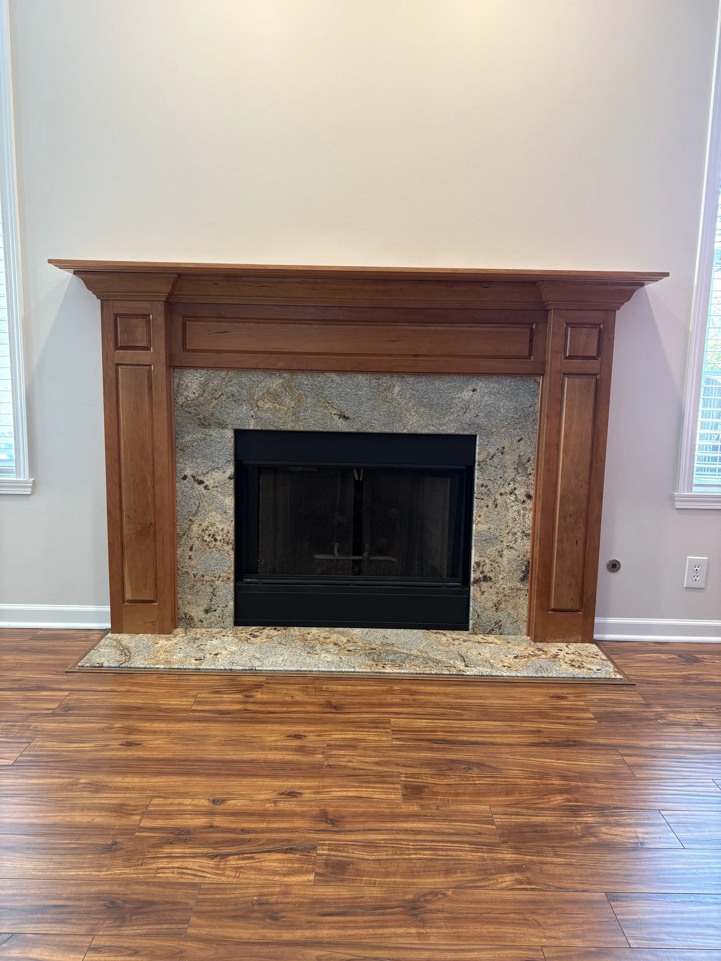 cherry wood fireplace mantel with raised panels in a beige room with stone hearth, wood floors, and white baseboard