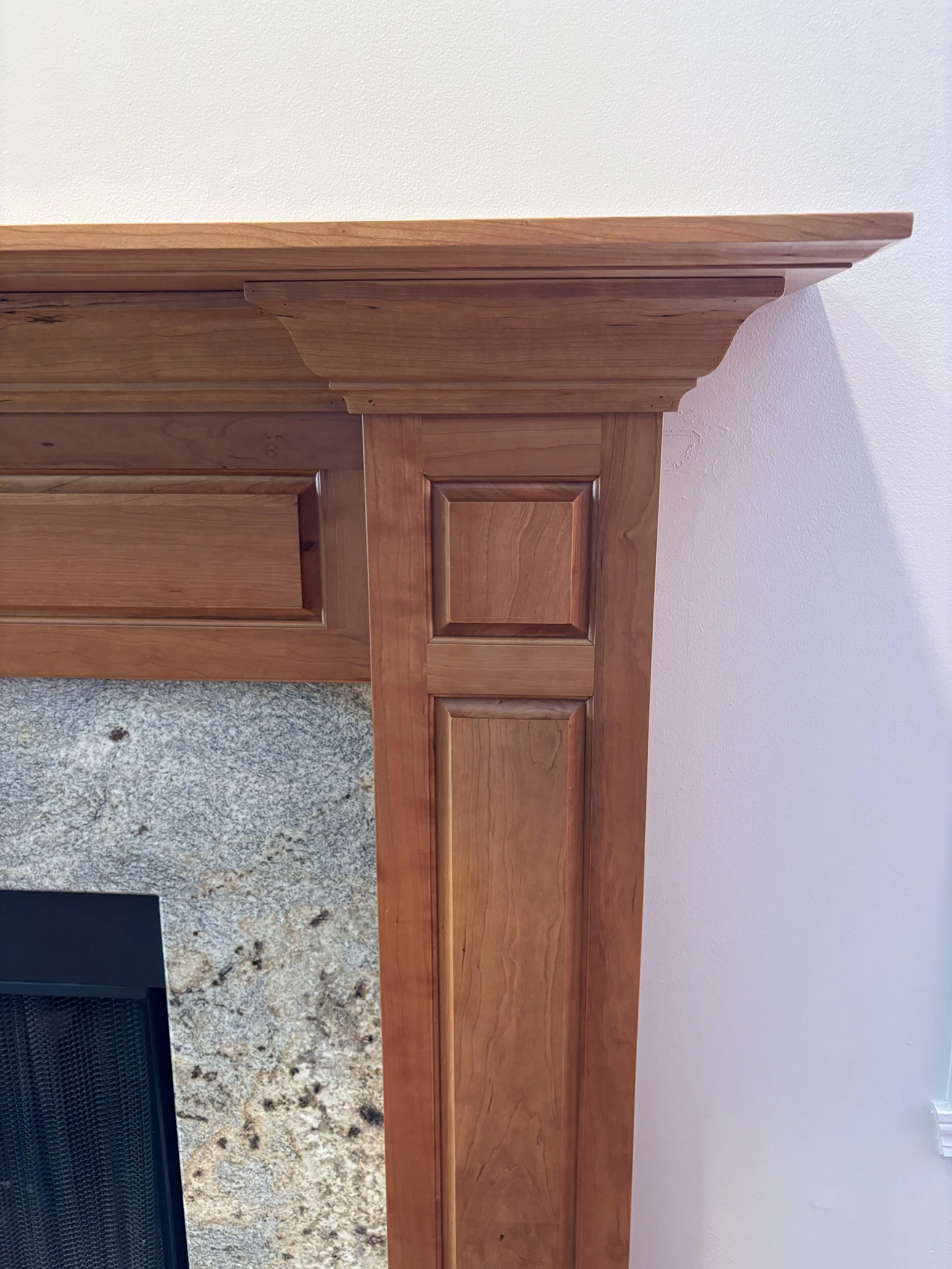 cherry wood fireplace mantel with raised panels in a beige room with stone hearth