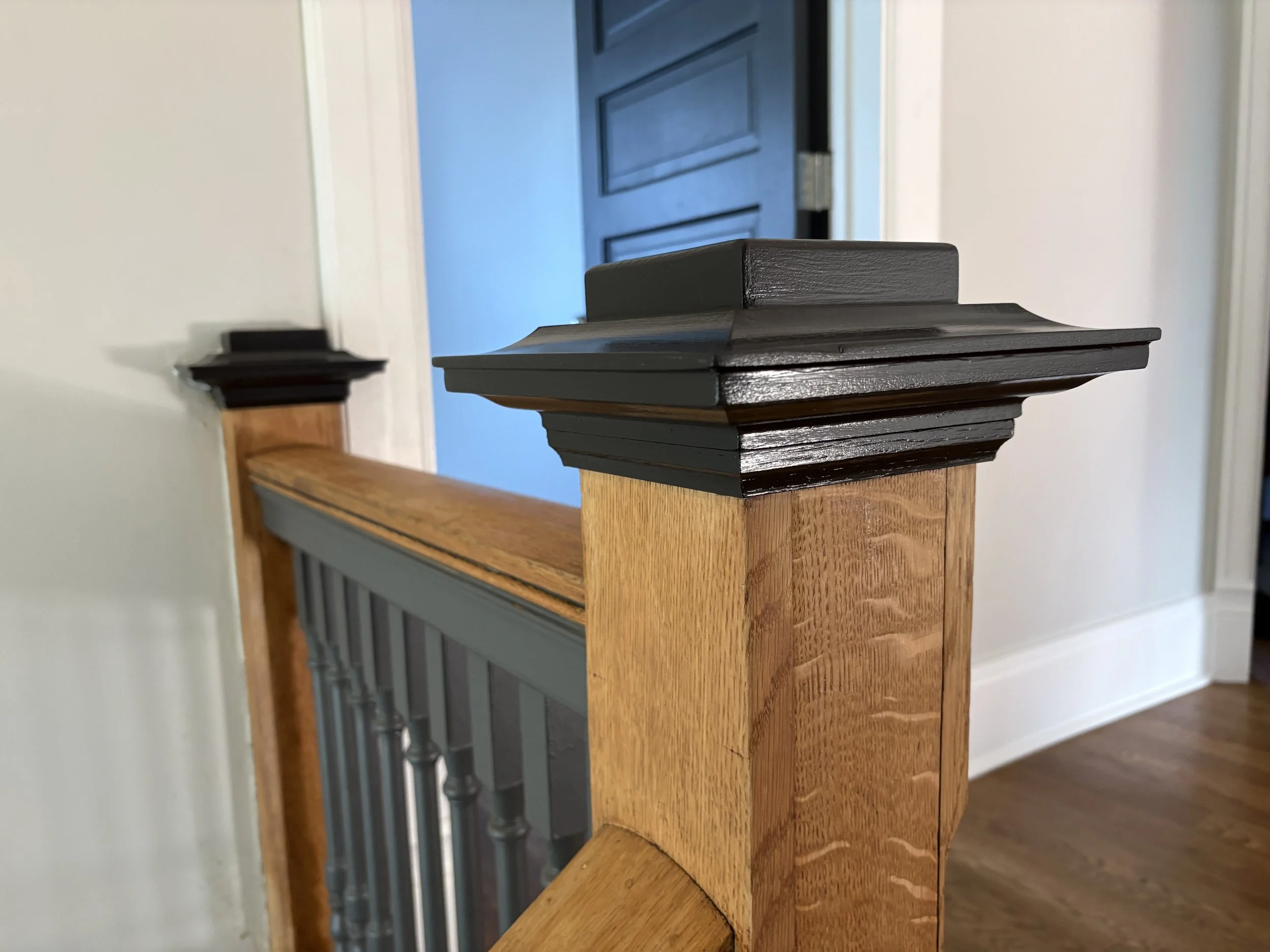black painted finial and trim on a newel post in a white room with hardwood floors