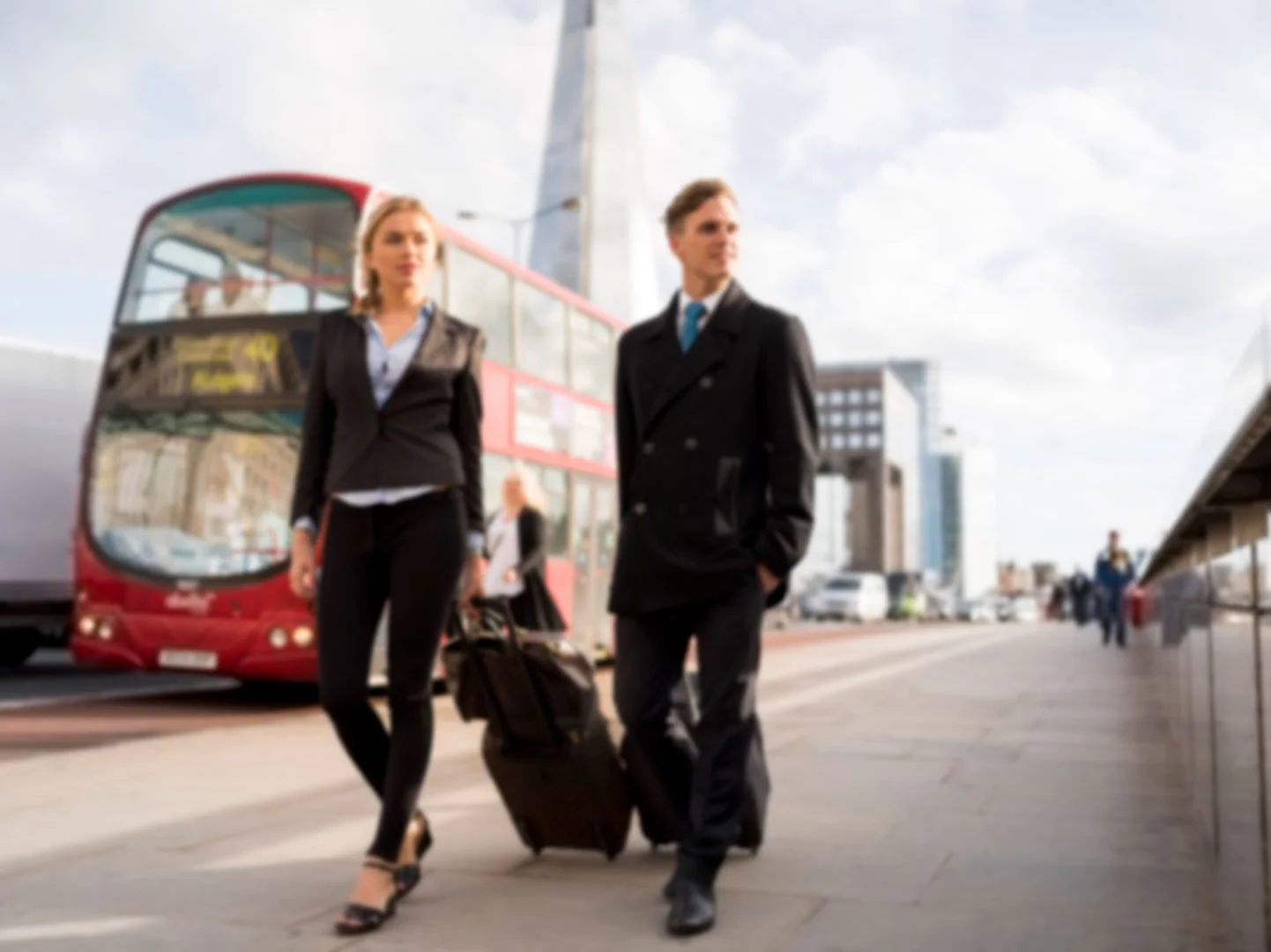 Two businesspeople, a woman and a man, walking near a double-decker bus and transportation hub in an urban area with skyscrapers.
