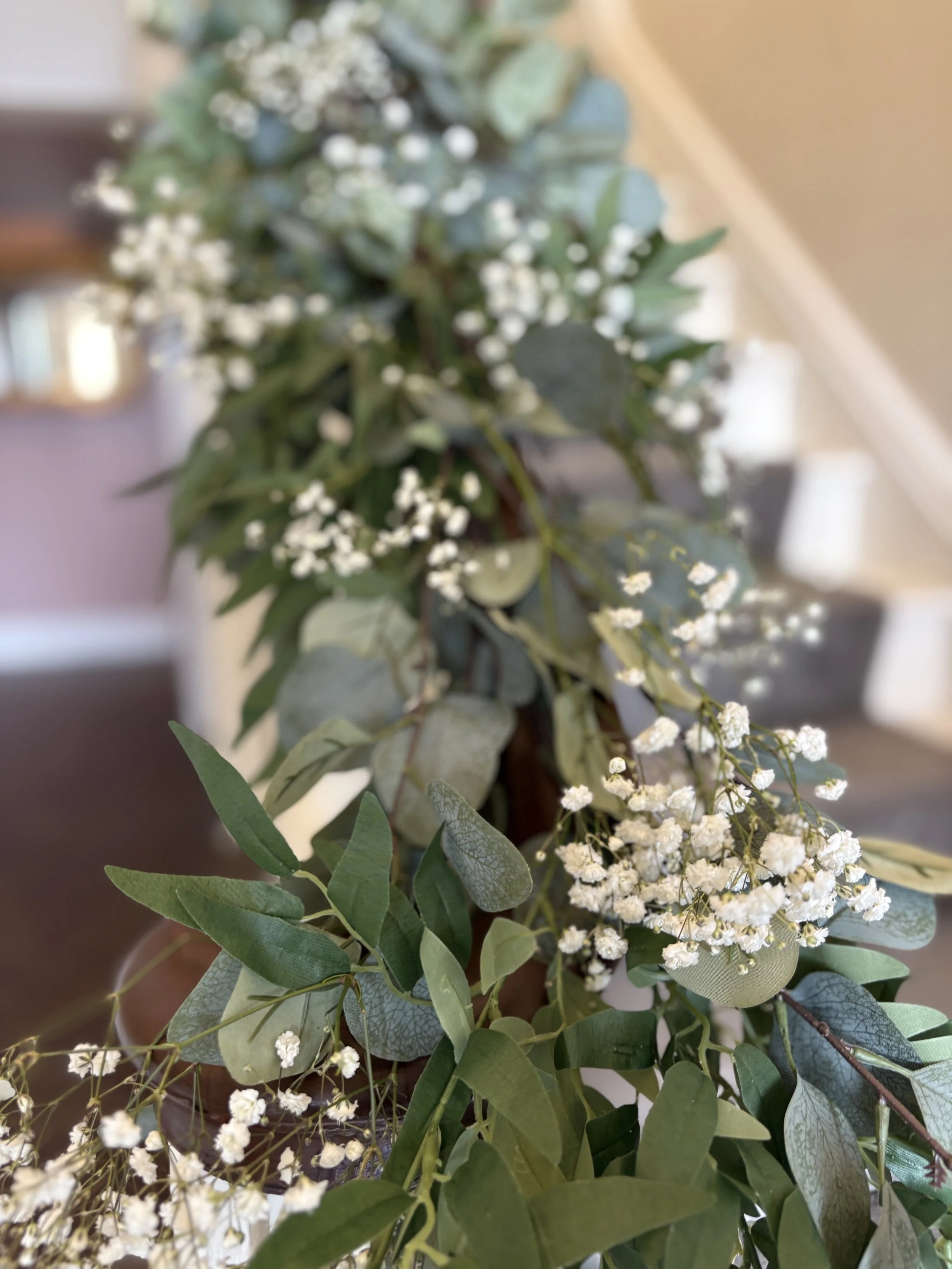 Close-up of a greenery and white flower arrangement on a brown table indoors.