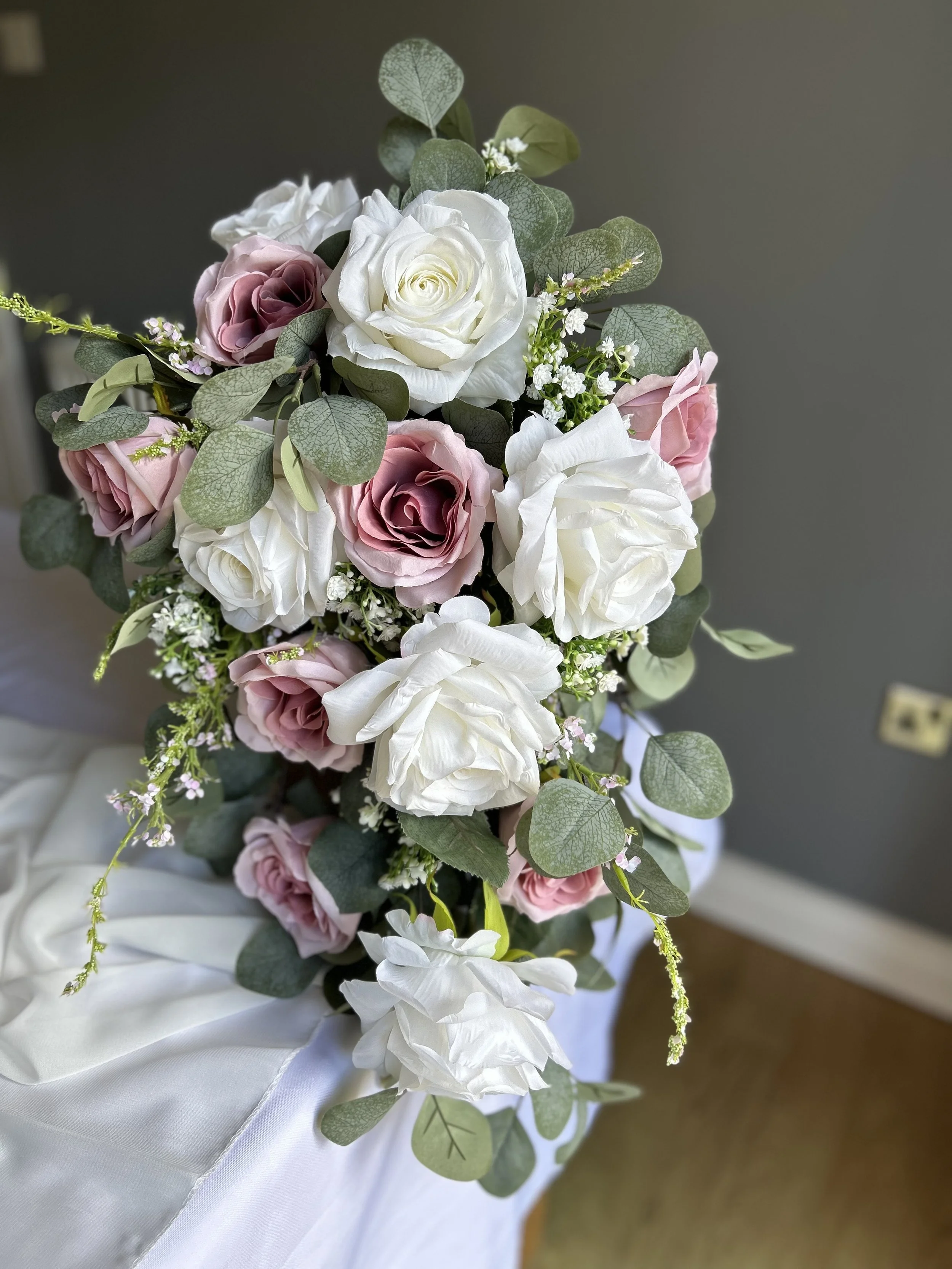 A bouquet of white and pink roses with greenery and small white flowers, placed on a white cloth surface.