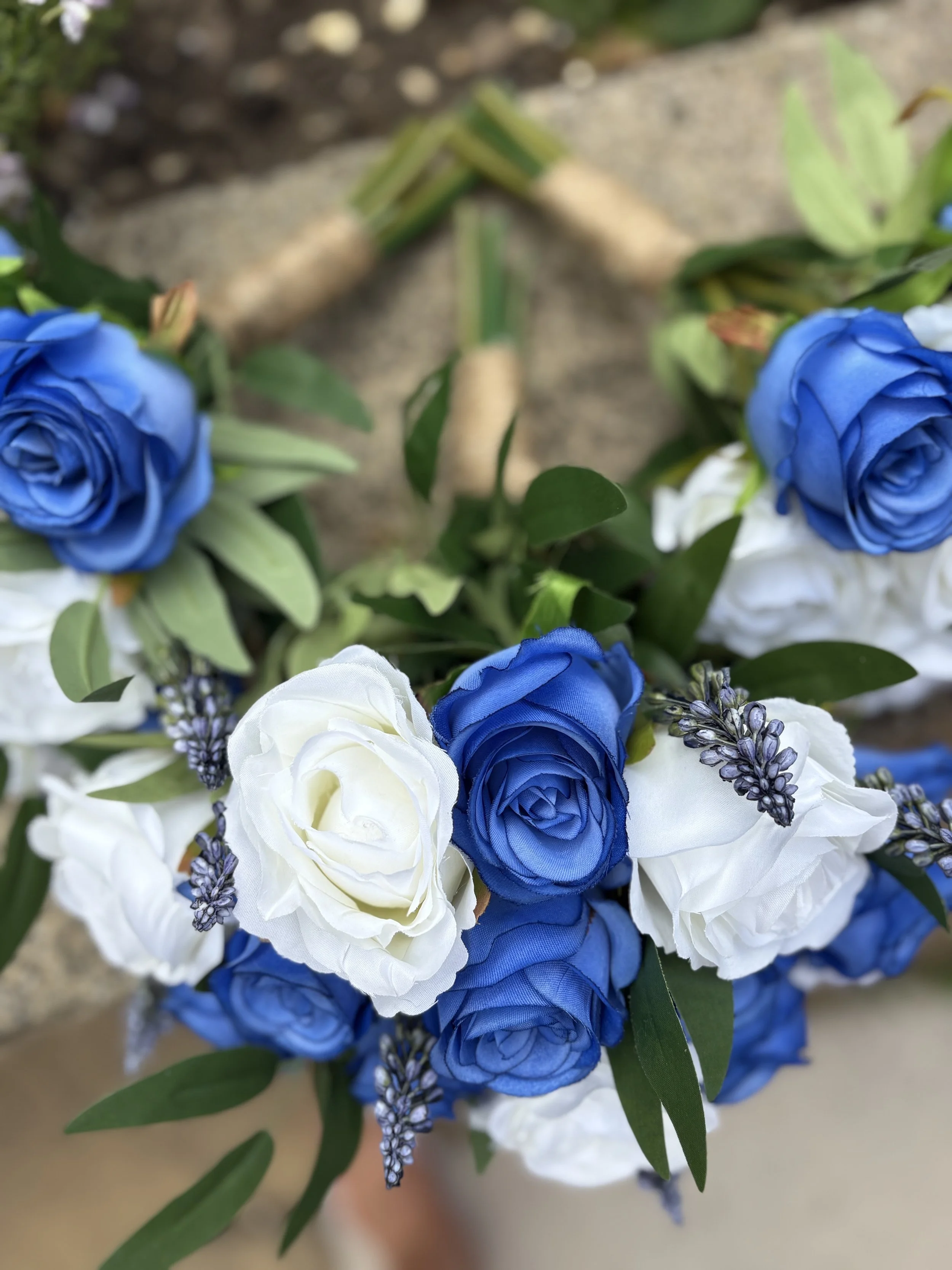 A close-up of a floral bouquet with white and blue roses, accentuated with purple lavender flowers and green leaves.
