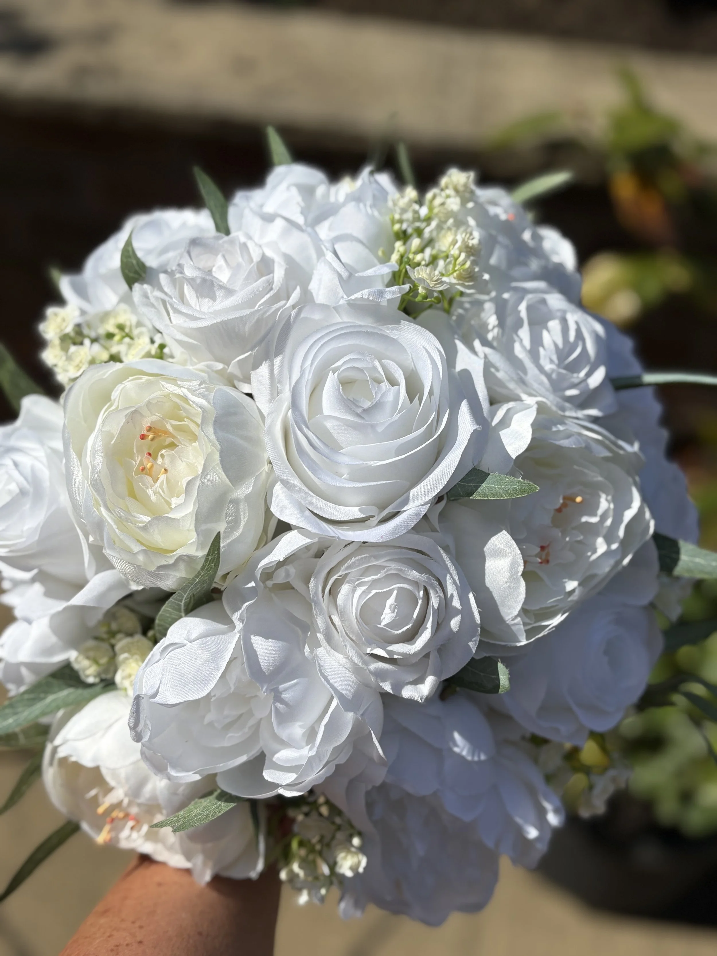 Close-up of a bouquet of white roses and other white flowers with green leaves.