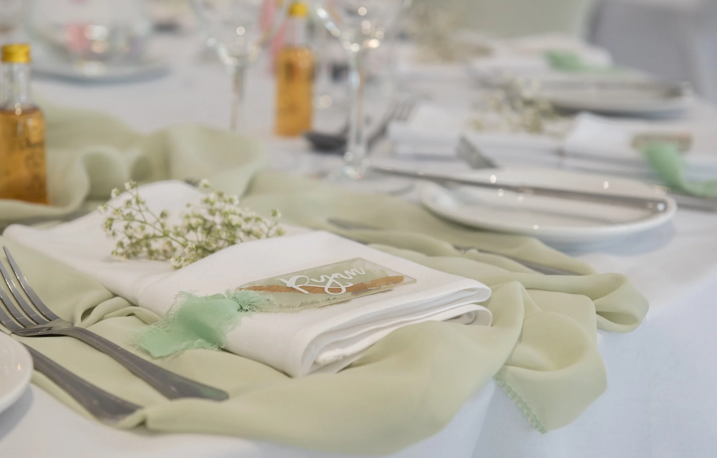 Elegant table setting with a white napkin, small flowers, and tableware, decorated with soft pastel-colored fabric.