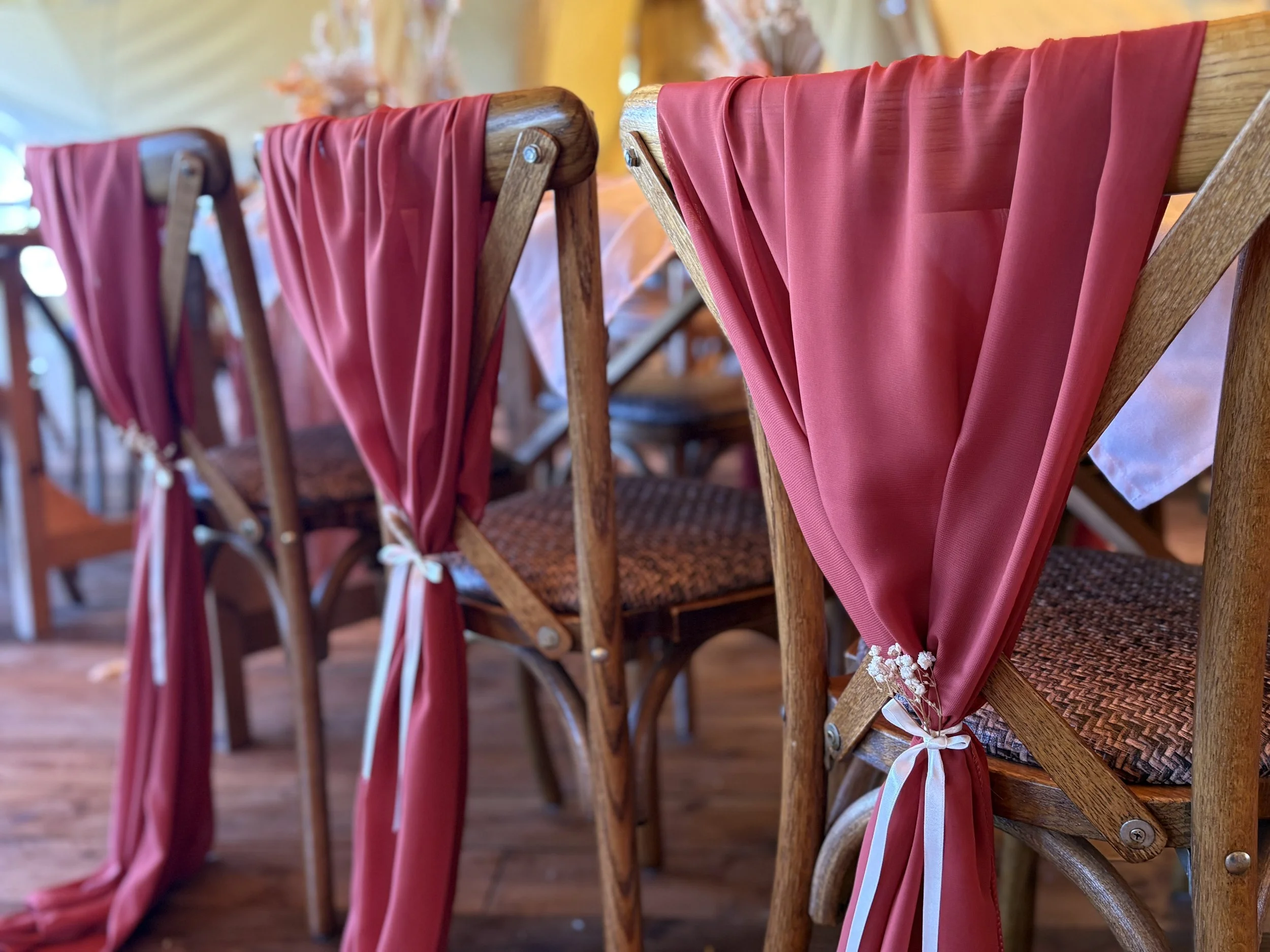 Wooden chairs with pink fabric draped over the backrests, tied with white ribbons, set in a formal dining setting.