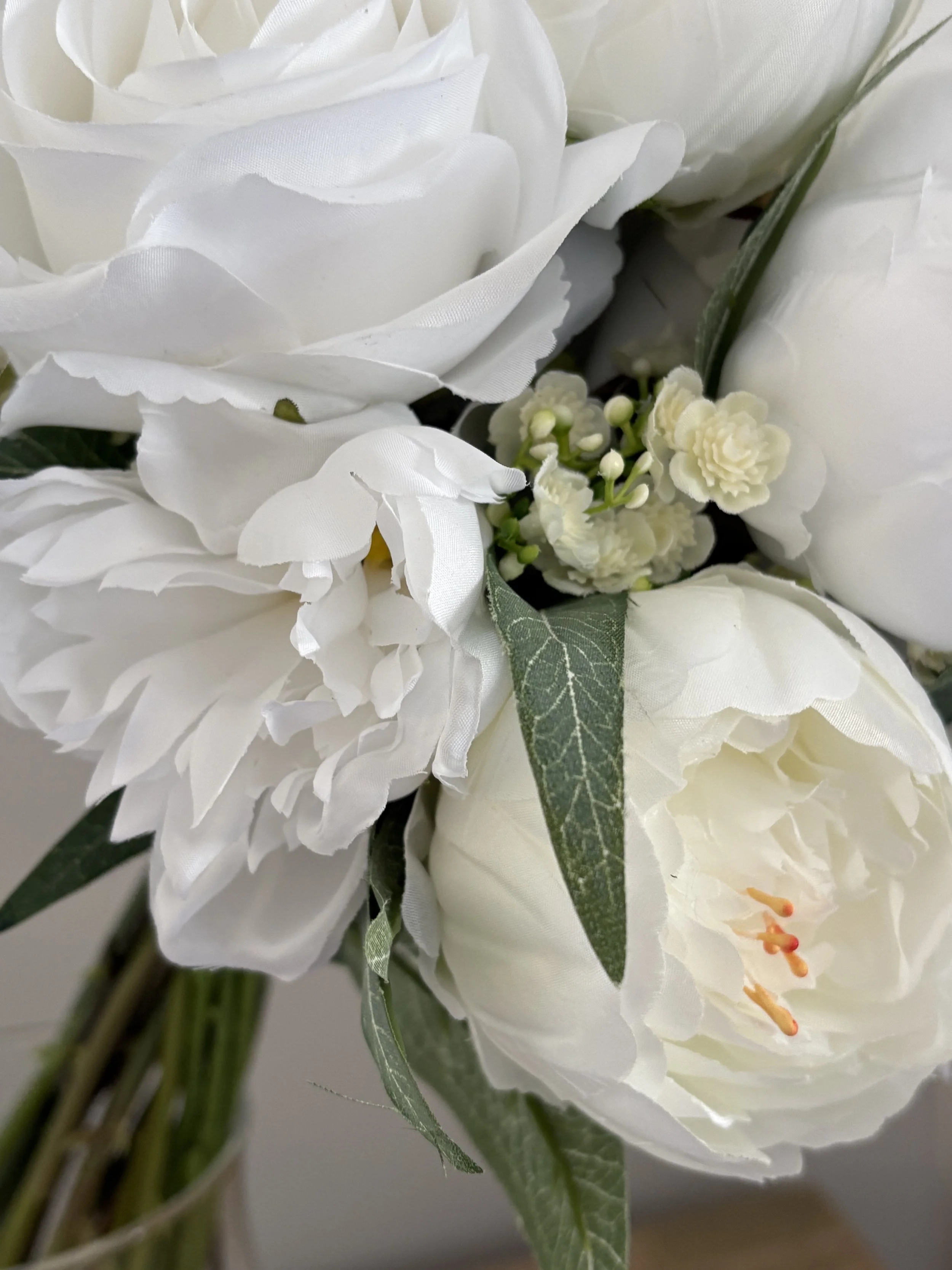Close-up of a bouquet of white artificial flowers, including large roses, small carnations, and greenery.