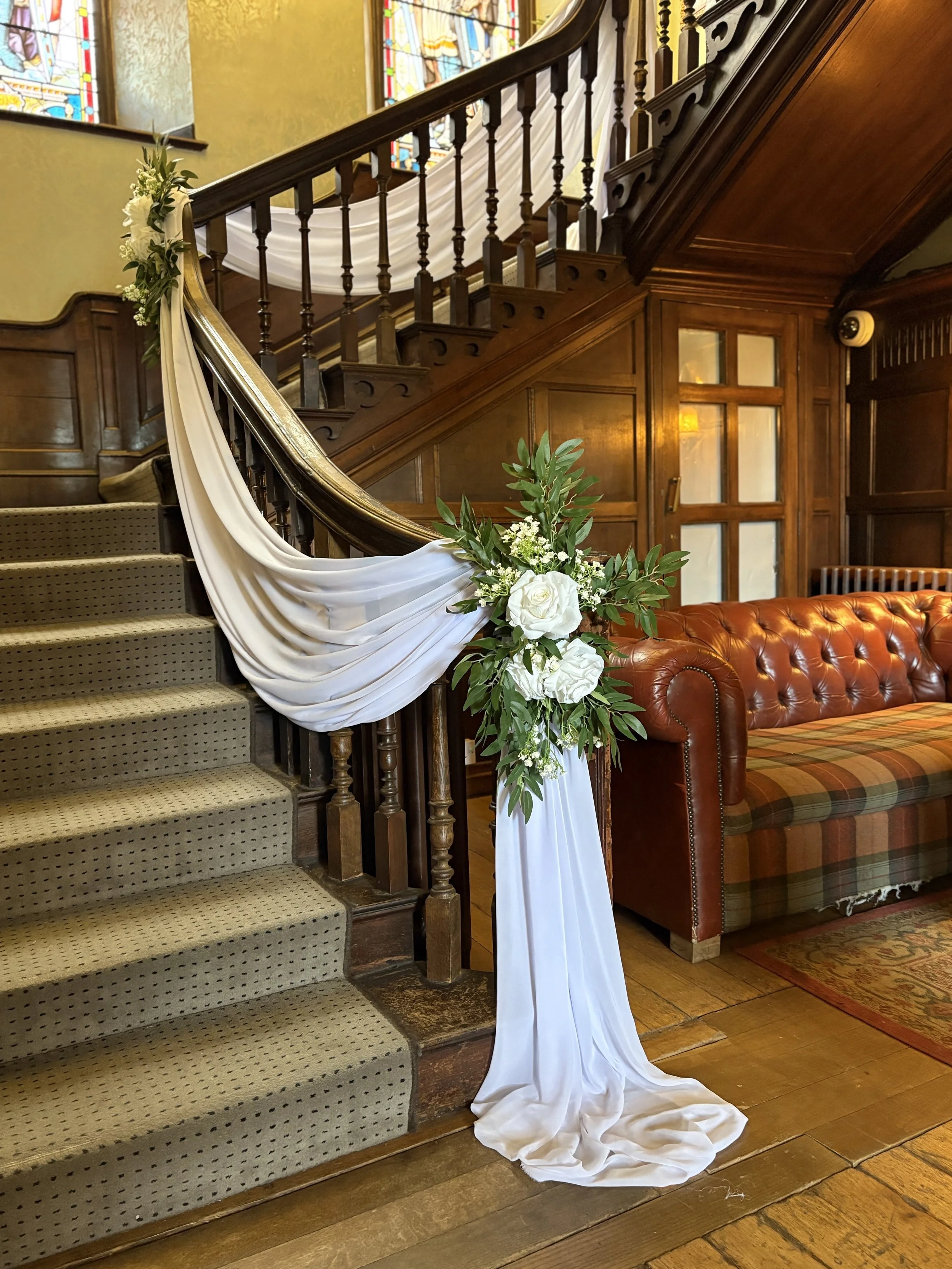 Dream Decor_Rothley Court_grand staircase styled with pristine white chiffon draped softly to give a dreamt look complimented with floral and foliage arrangements to complete the look