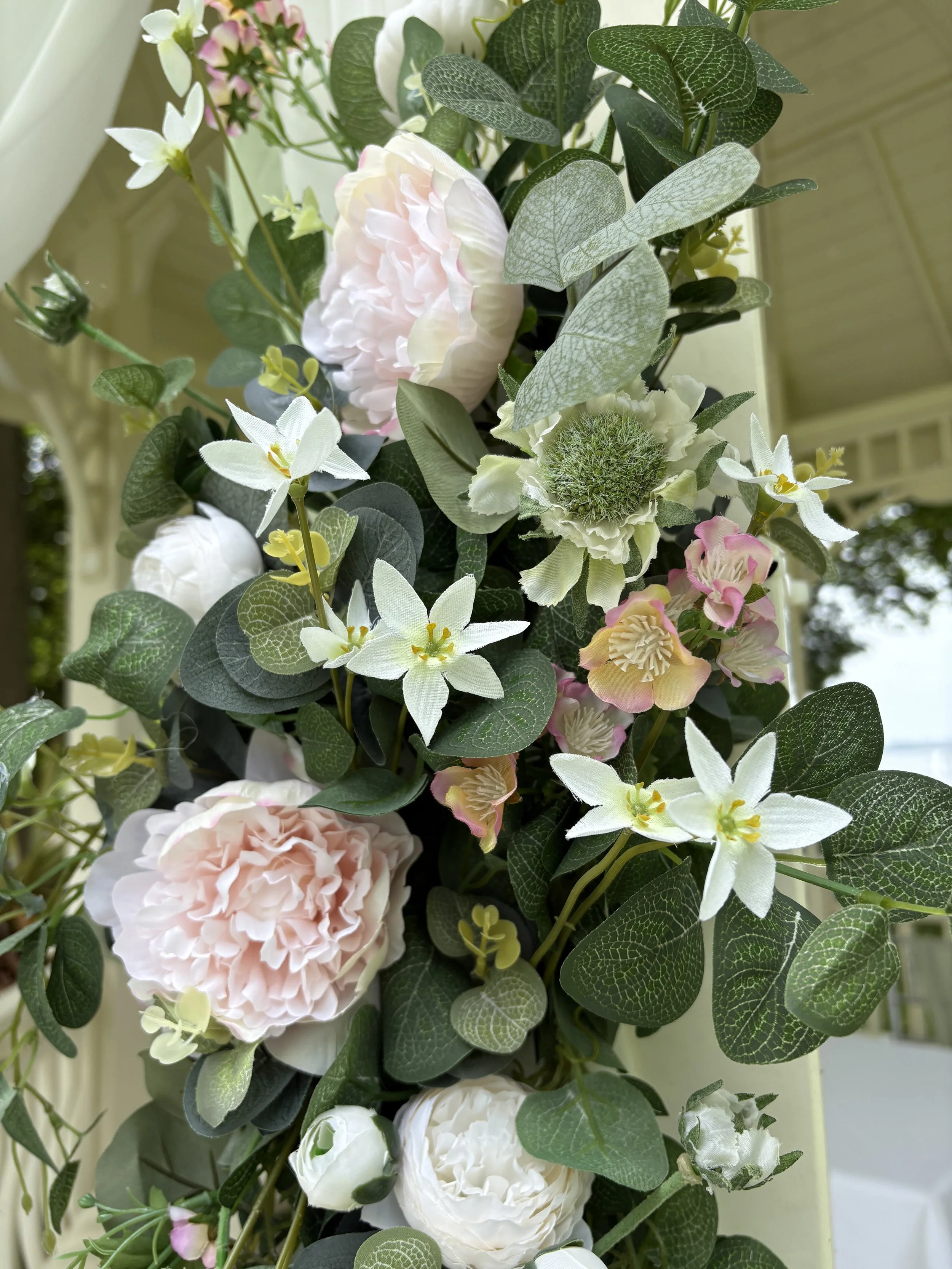 Close-up of a floral arrangement with pink peonies, white orchids, and various green foliage.