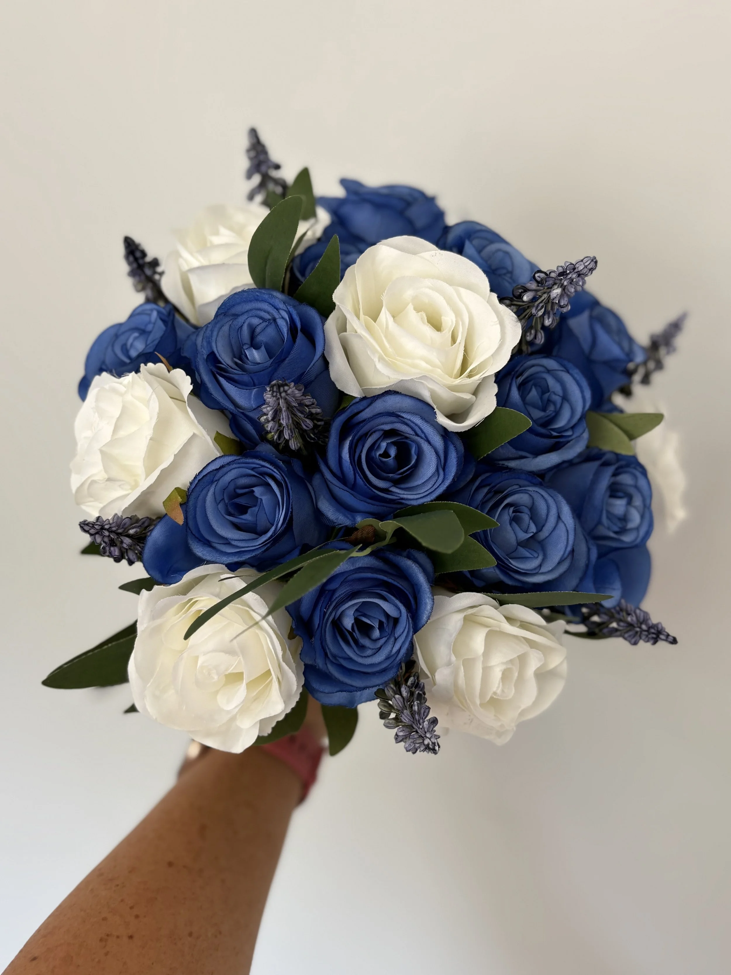 A bouquet of blue and white artificial roses with greenery and small purple flowers.