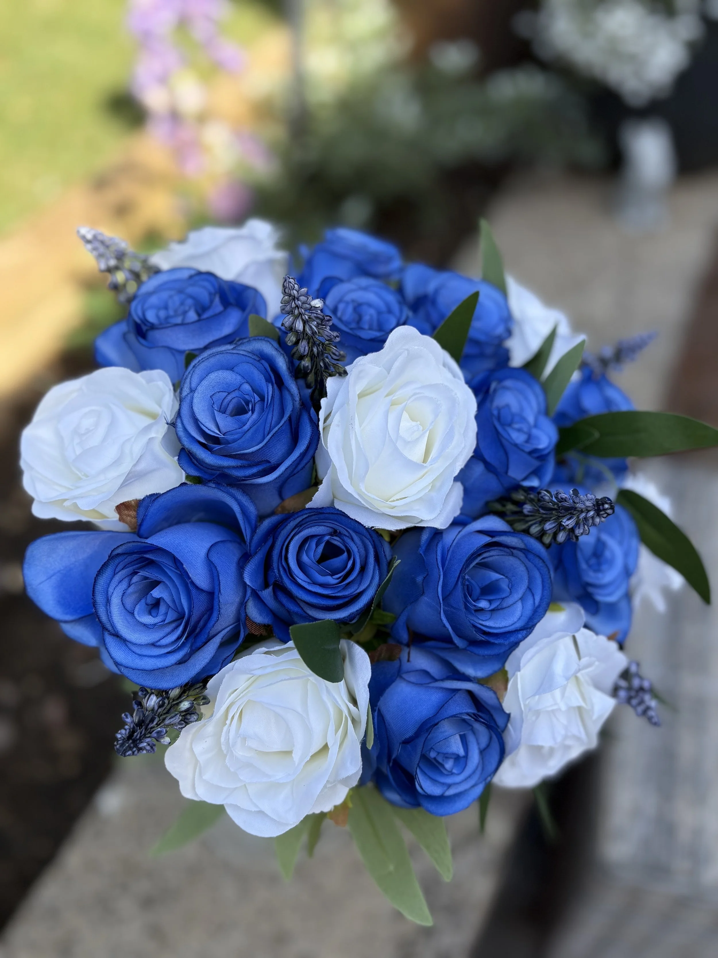 A bouquet of blue and white roses with purple accent flowers and green leaves.