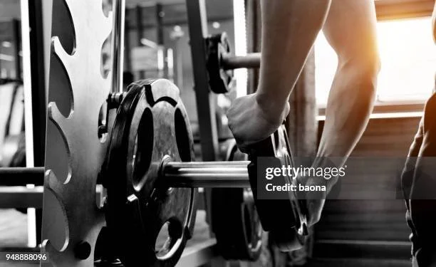 Person lifting a barbell with weight plates in a gym.
