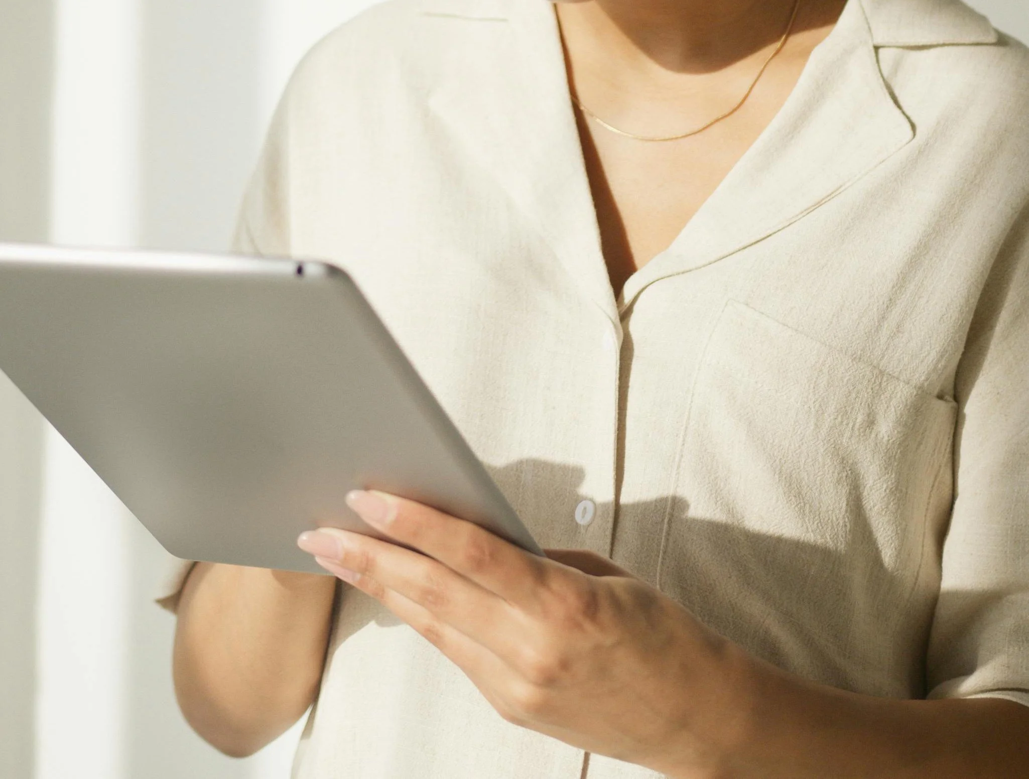 Person holding a tablet device wearing a cream-colored shirt and gold necklace.