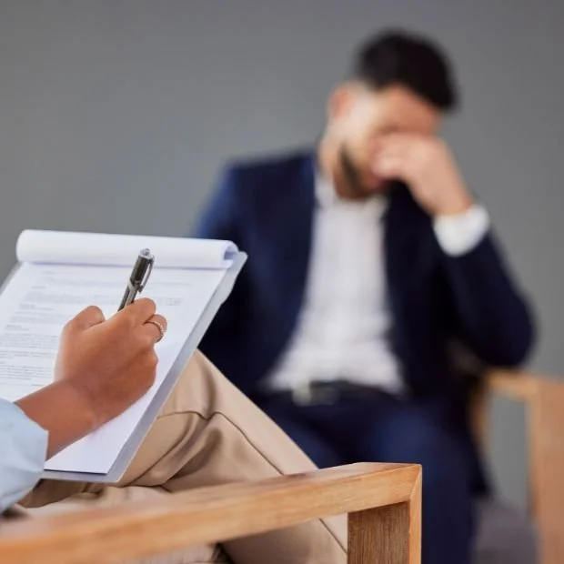 Hombre en una sesión de terapia, con un profesional tomando notas.