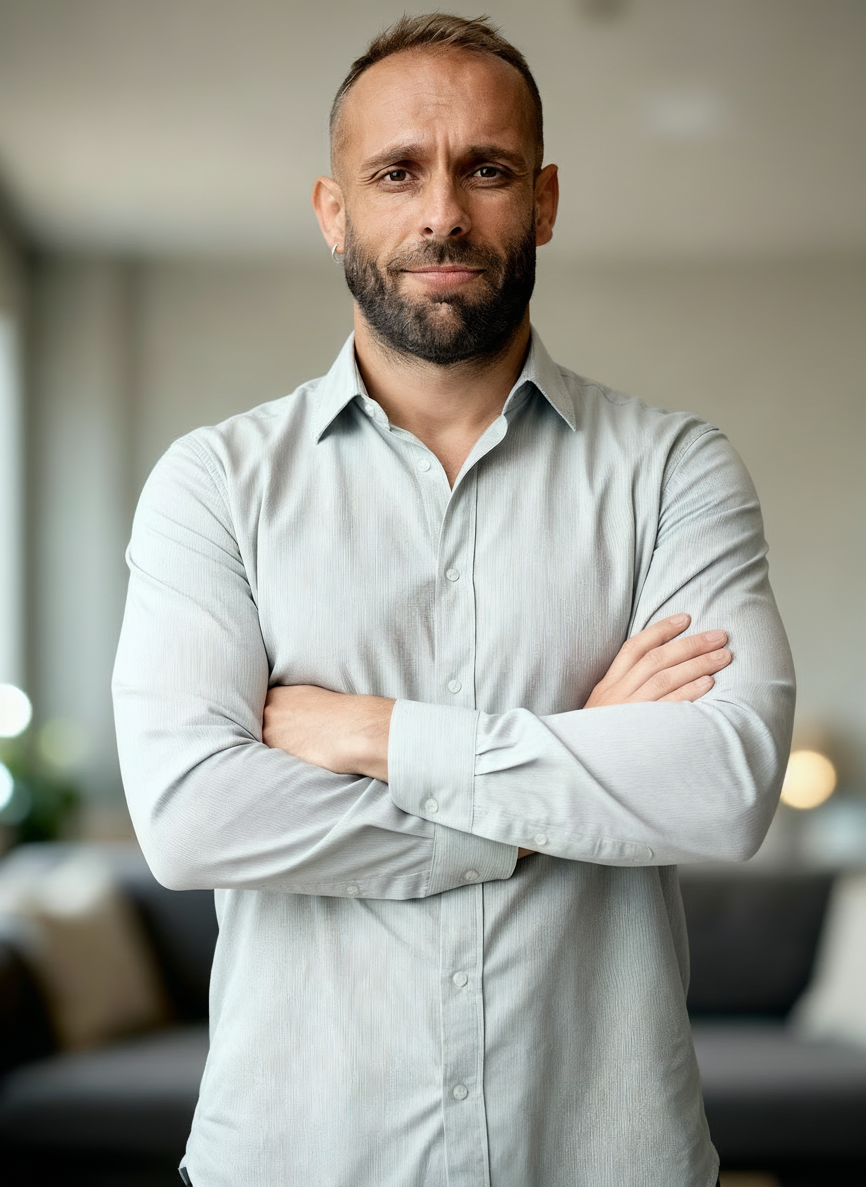 Retrato de un hombre con barba y cabello teñido, usando camisa gris, en un ambiente de oficina.
