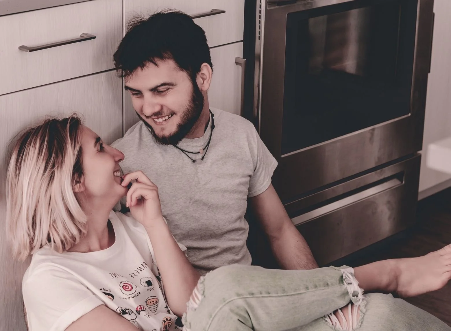 Una pareja sentada en el suelo de la cocina, sonriendo y mirándose con cariño.