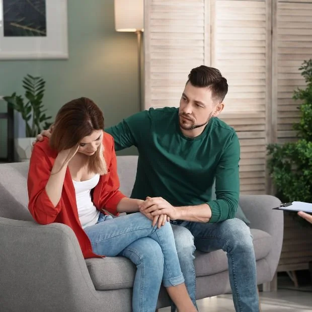 Un hombre consuela a una mujer que parece llorar en una sesión de terapia o consejería en un salón cómodo.