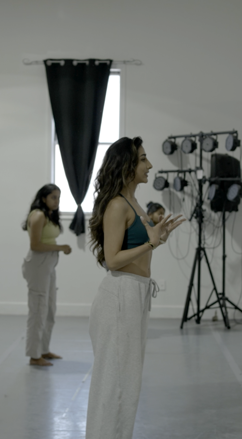 Women practicing dance or movement in a studio, with lights and equipment in the background.