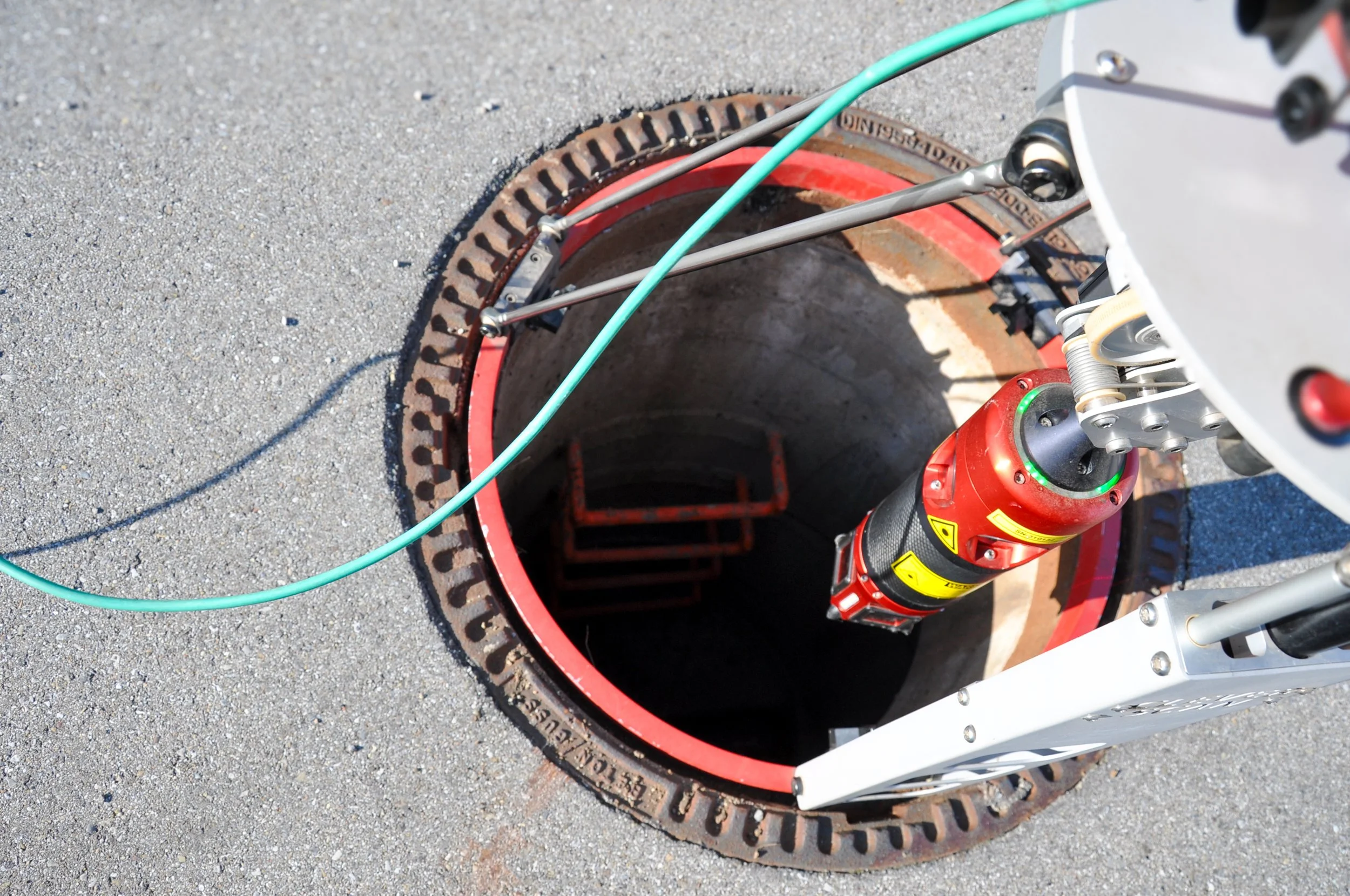 Eine Clever Scan Schacht Kamera, die in einen Schacht abgelassen wird, mit sichtbarem Kamera Kopf, umgeben von Sicherheitsvorrichtungen und Kabeln.