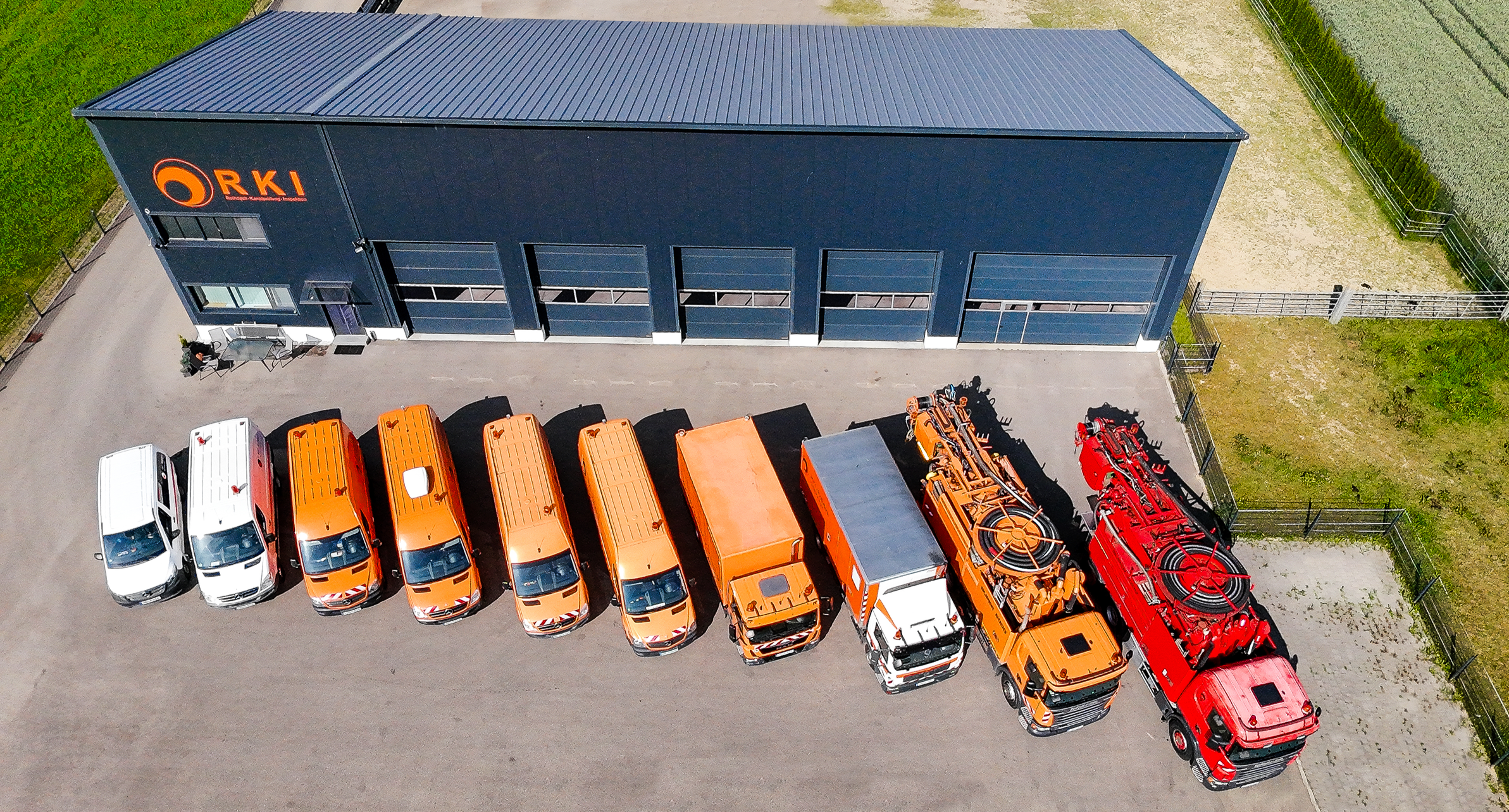 Luftaufnahme des RKI Firmengebäudes mit orange und roten Kanalreinigungsfahrzeugen vor der Fassade, die das Logo 'RKI' trägt.