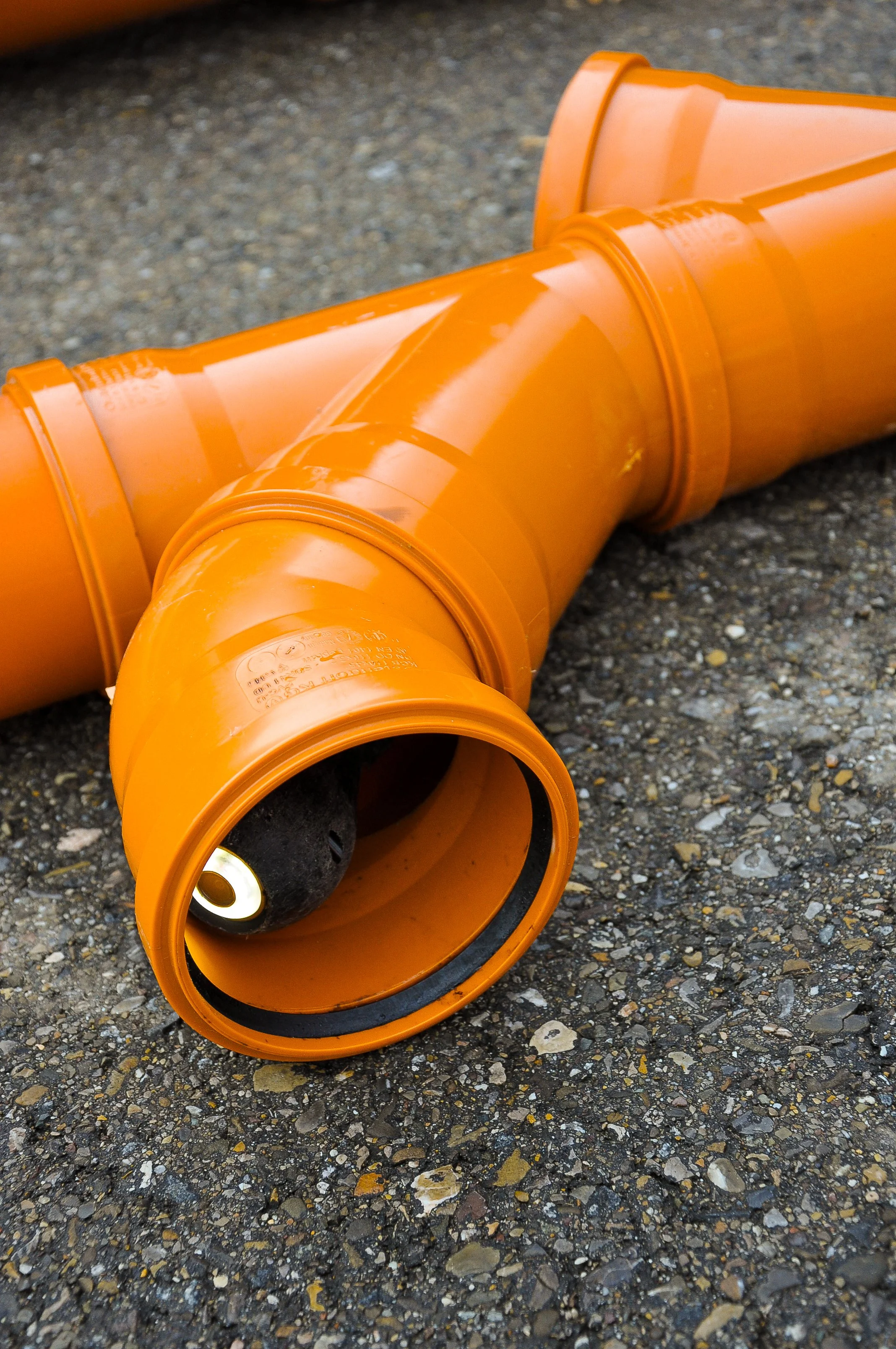 Ein orangefarbener Rohrbogen aus Kunststoff auf Asphalt.