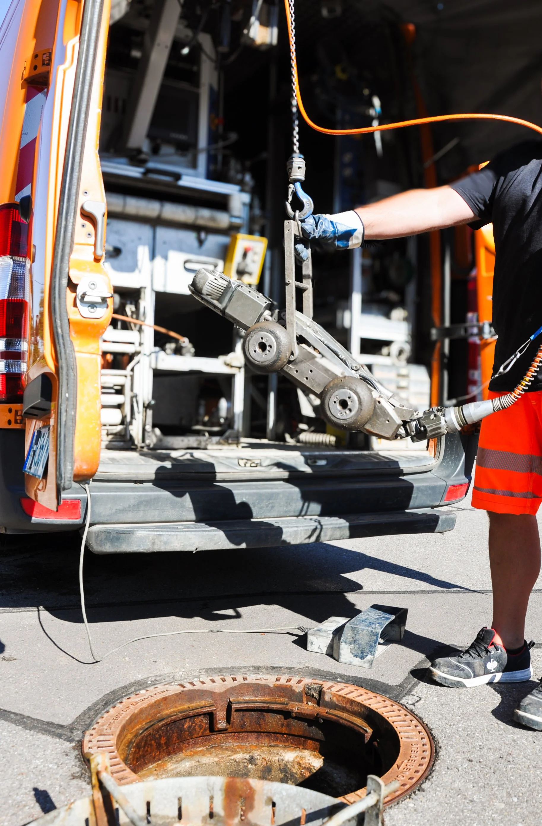 Ein Techniker hebt eine Rohrreinigungsmaschine aus einem Servicewagen, um ein geöffnetes Abwasserrohr im Boden zu reinigen.