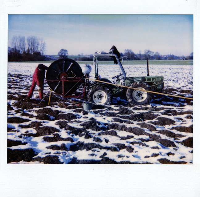 Landwirtschaftlicher Traktor in einem verschneiten Feld mit einer Person in roter Kleidung, die Kanäle reinigt.
