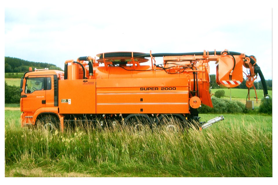 Ein orangefarbiger Kanalspüler mit der Beschriftung 'Super 2000', der auf einer grünen Wiese im Freien steht.