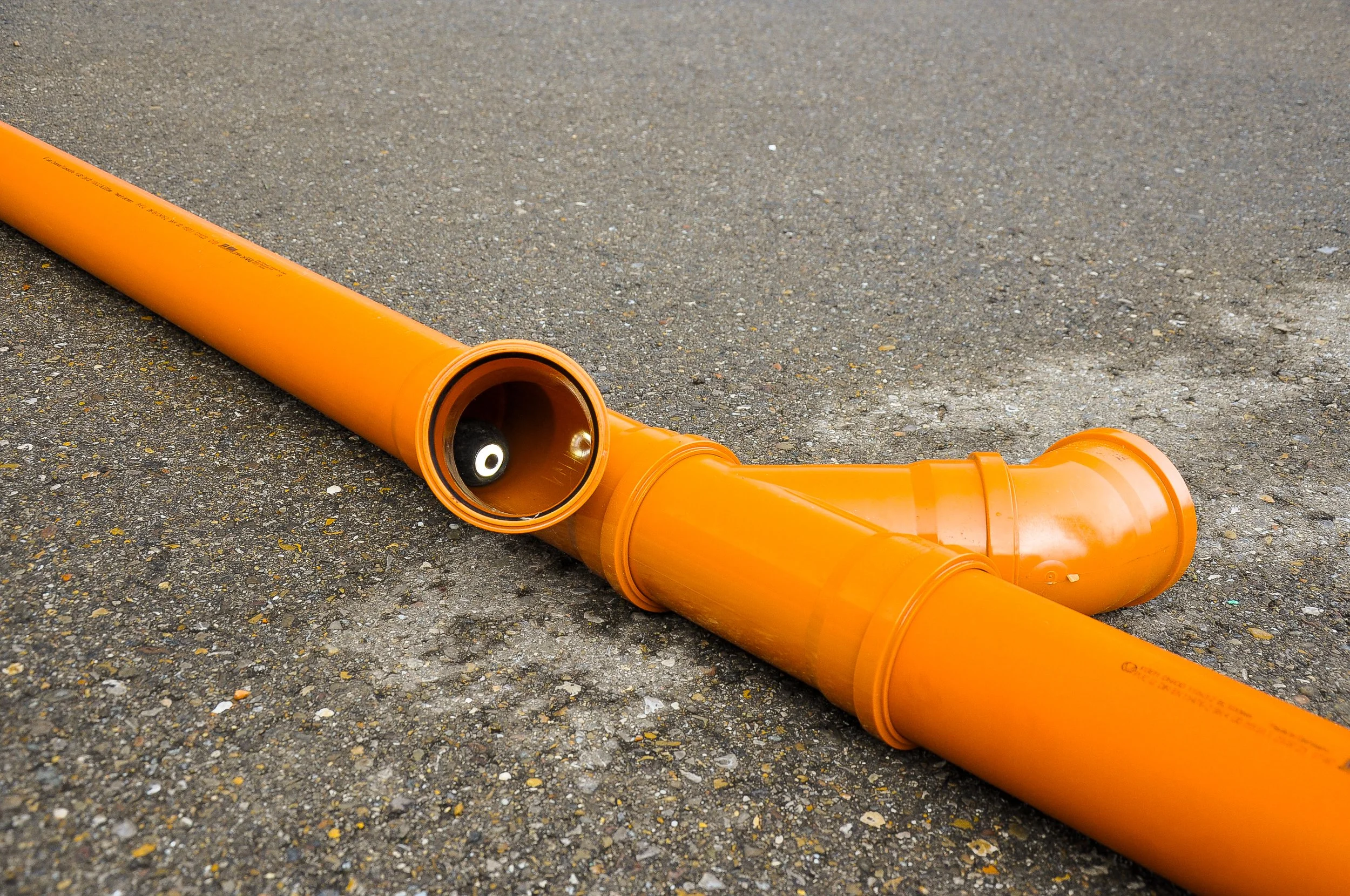Ein orangefarbener Abwasserrohr auf asphaltierter Straße.