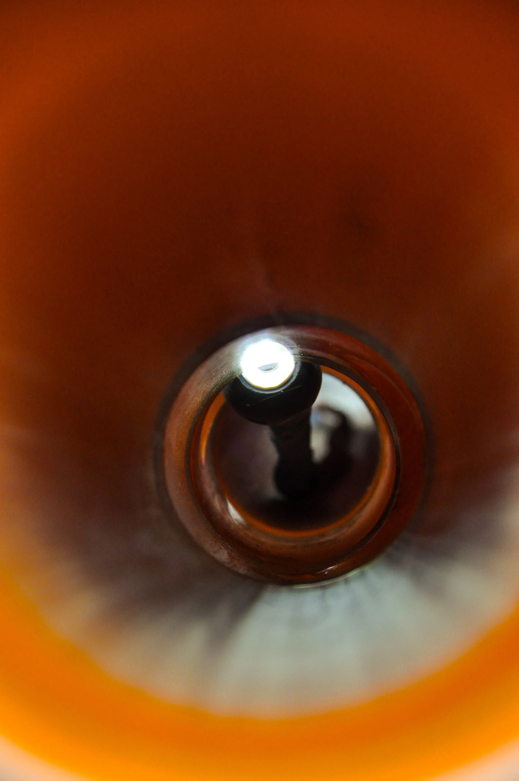 Innenansicht eines Flaschenhalses, Blick nach unten in die Flasche mit dunklem Inhalt, Lichtquelle sichtbar am Flaschenhals