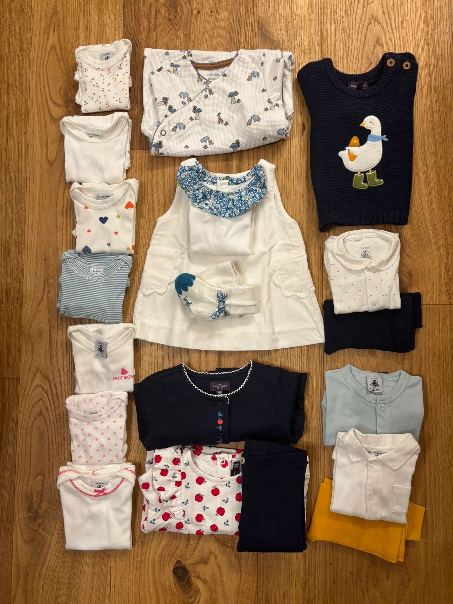 Collection of children’s clothing including shirts, dresses, and pajamas in various colors and patterns laid out on a wooden floor.