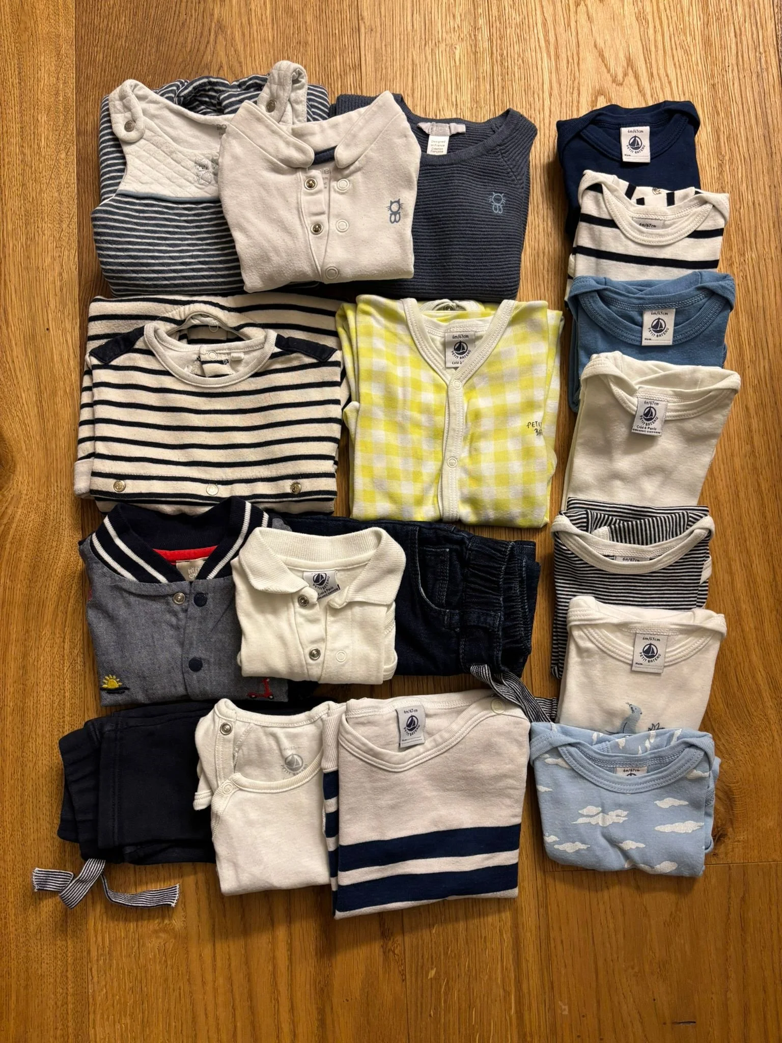 Collection of folded children's clothing, including various shirts, sweaters, and onesies with different patterns and colors, laid out on a wooden surface.