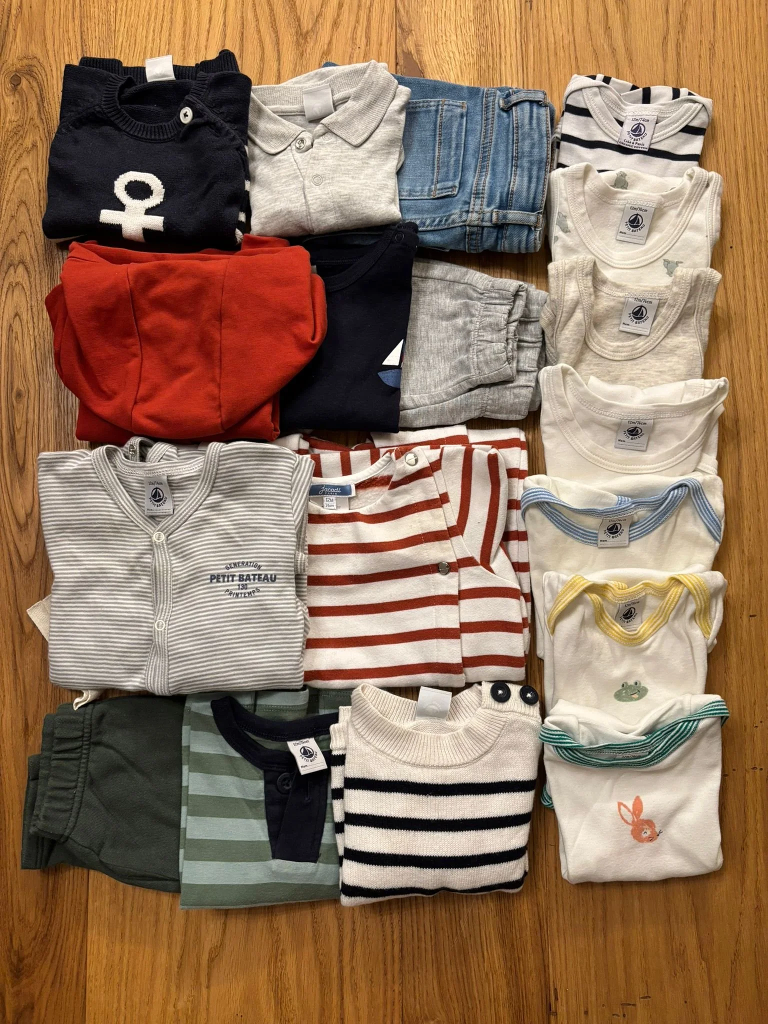 Collection of children's clothing including shirts, pants, and sweaters, neatly folded and arranged on a wooden surface.