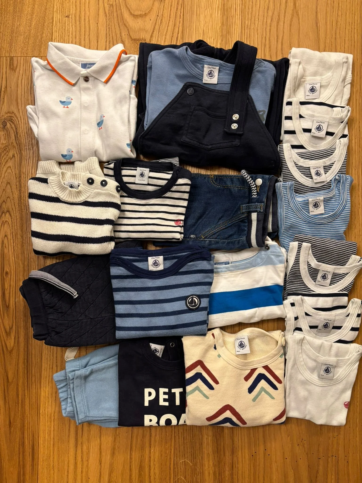 Collection of children's clothing including shirts, sweaters, pants, and pajamas arranged on a wooden surface.