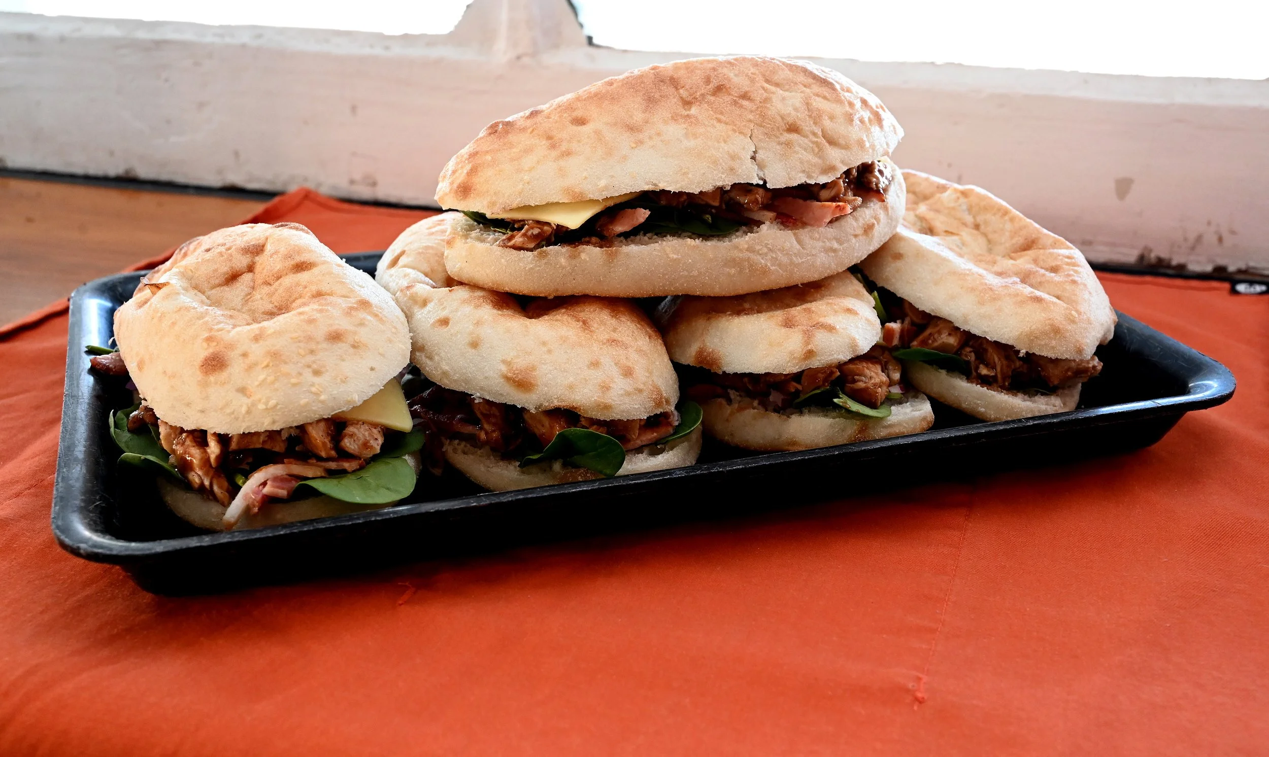 Several Italian-style po' boy sandwiches with bread, roasted meat, cheese, and greens on a black tray.