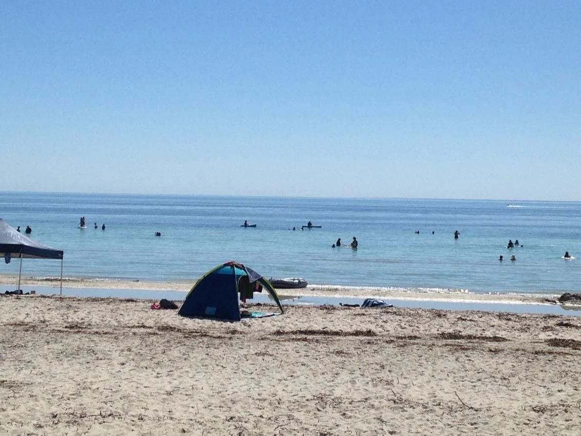 Beach scene with a tent and people swimming and boating in the ocean.