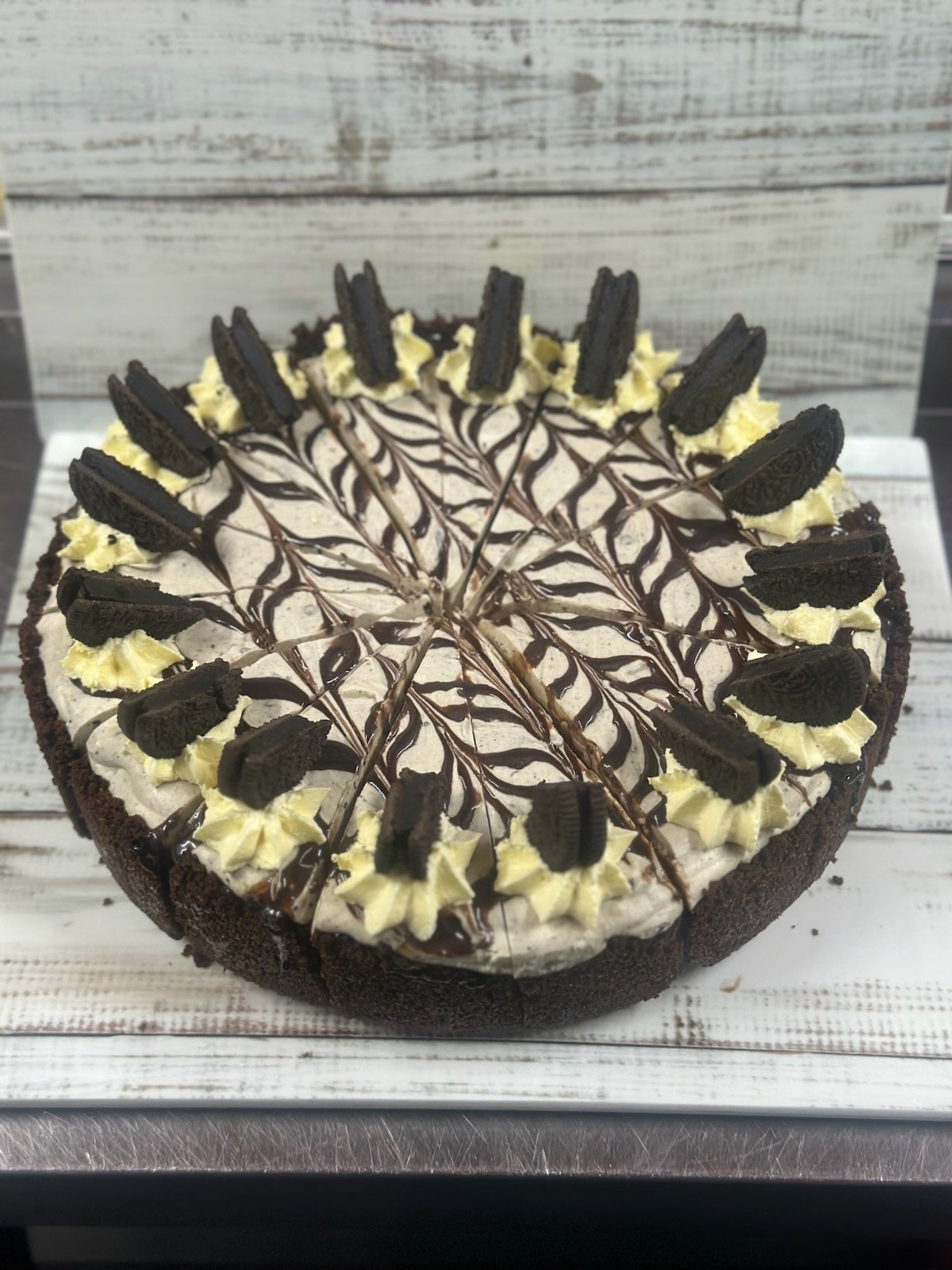 Our Oreo chocolate cake decorated with Oreo cookies and piped cream on top, drizzled with chocolate sauce in a circle pattern.