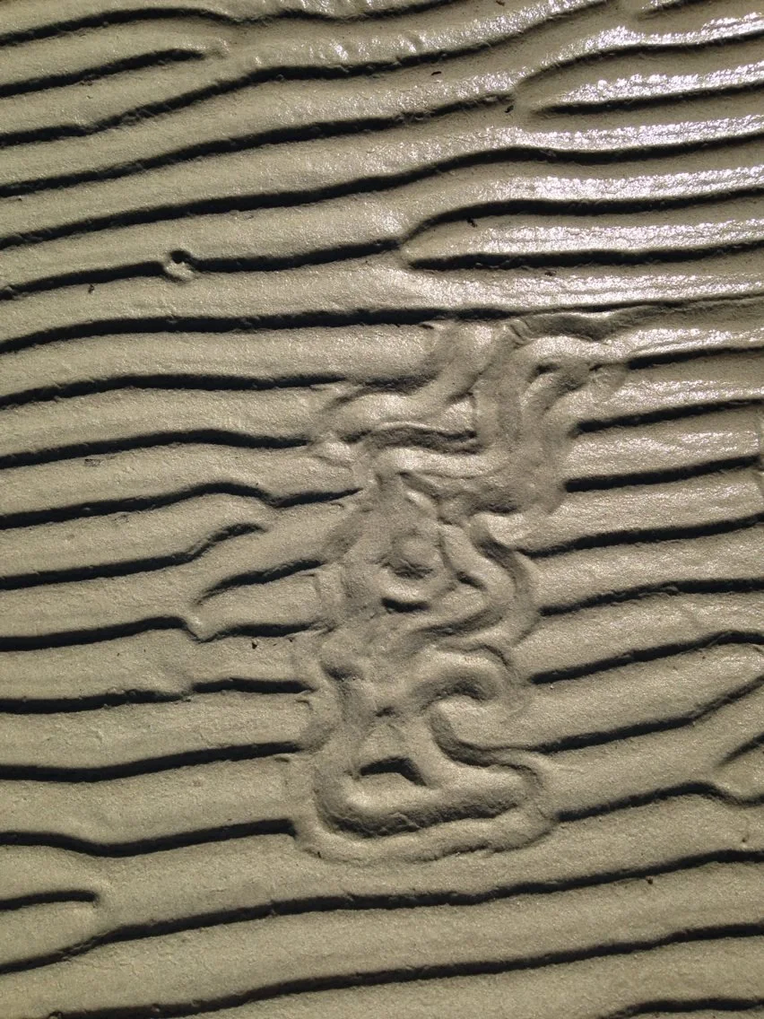 Close-up of a textured sand surface with a dragon-shaped design etched into it.