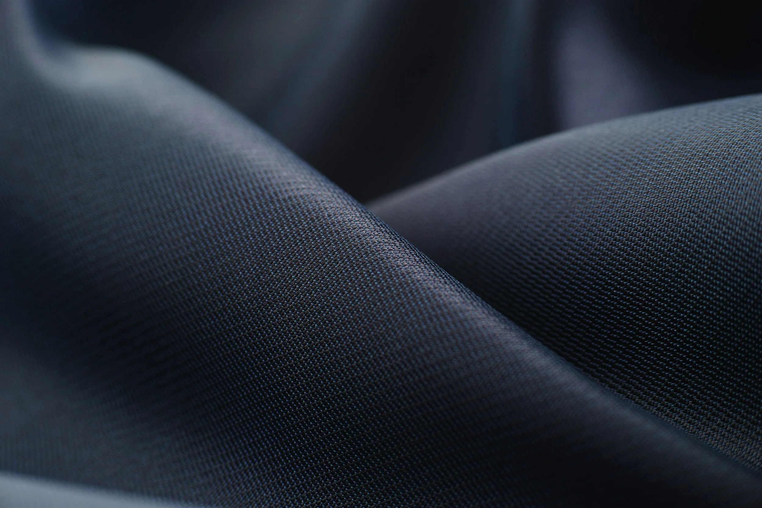 Close-up view of textured black or dark blue fabric showing fine woven pattern with soft light highlighting the surface
