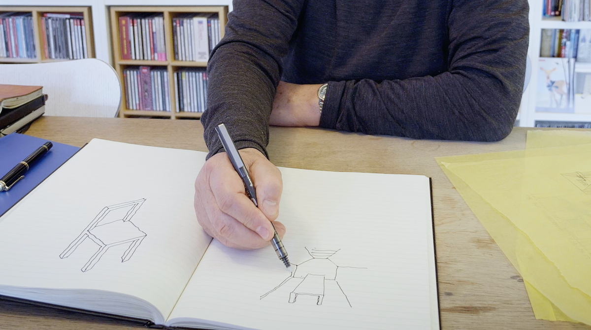 Person sitting at a desk drawing sketches of chairs in a notebook.