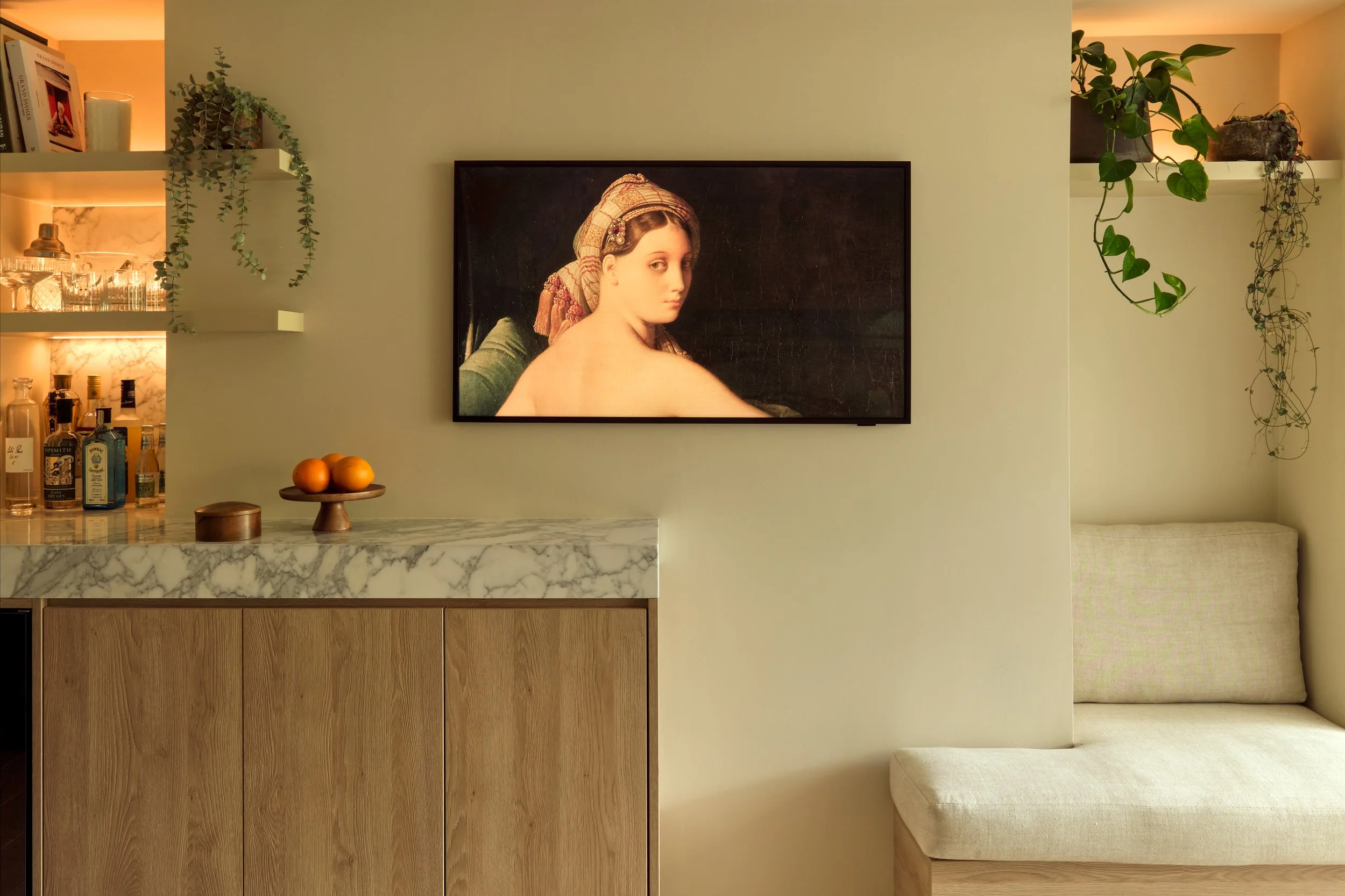 Interior of a modern living space with a marble-top cabinet, a framed classical painting of a woman on the wall, and decorative plants on shelves.