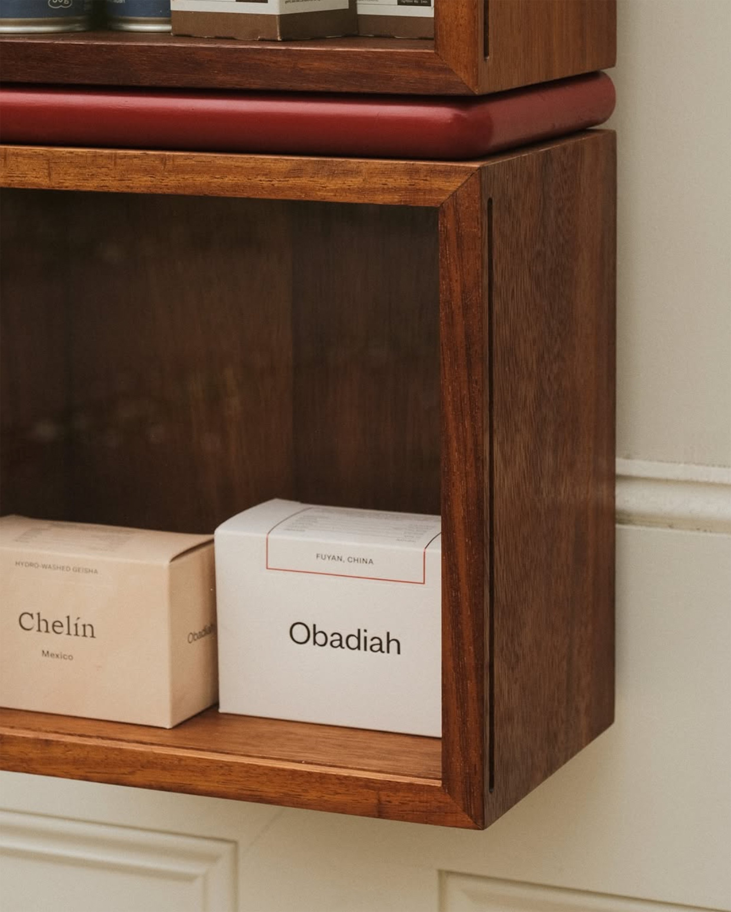 Two white boxes of herbal soap on a wooden shelf. One is labeled 'Obadiah' and the other 'Chelín', with the country of origin noted on each.
