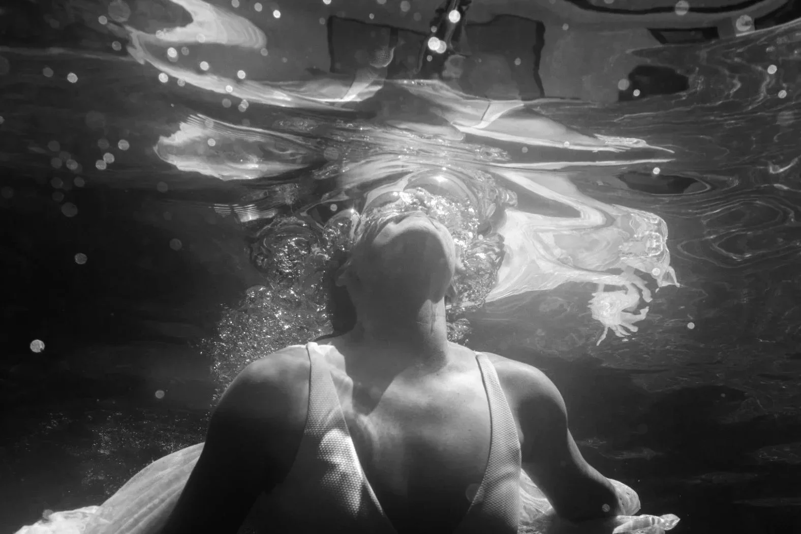 A woman in a swimsuit underwater, with her face tilted upward and bubbles surrounding her.