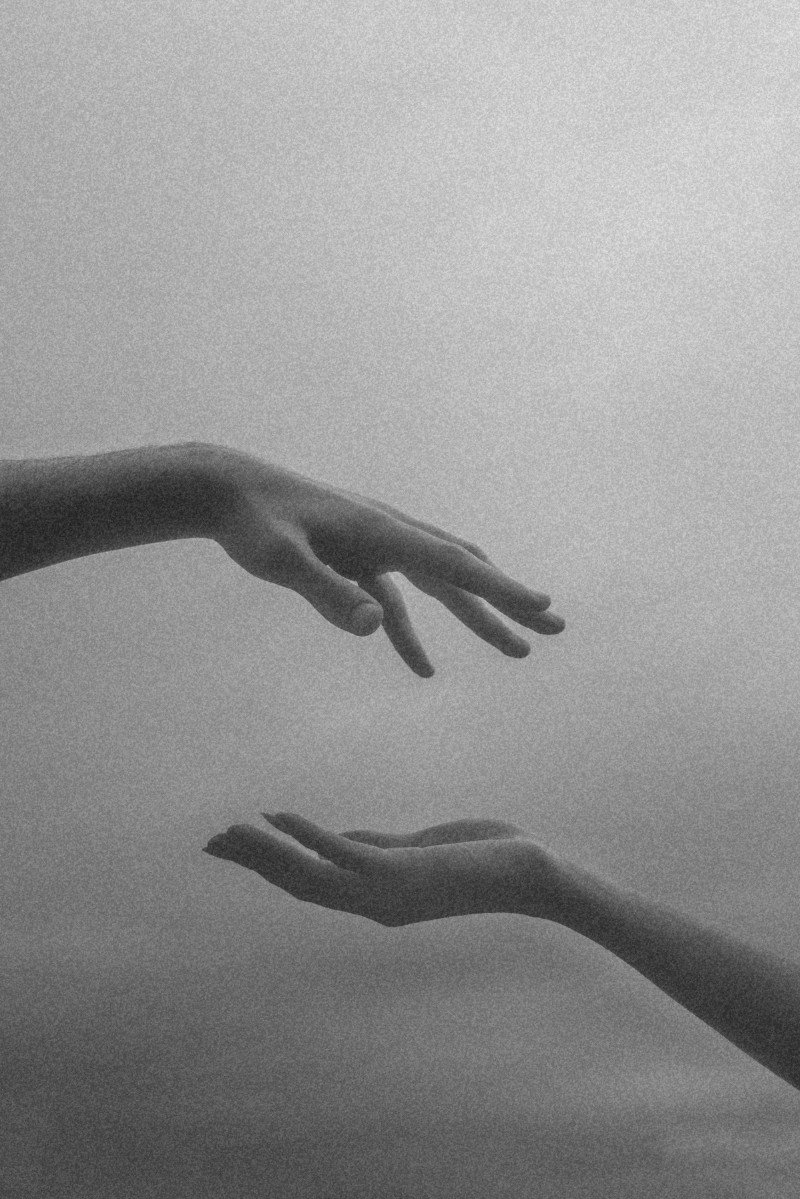 Two hands reaching towards each other in a black-and-white photograph.