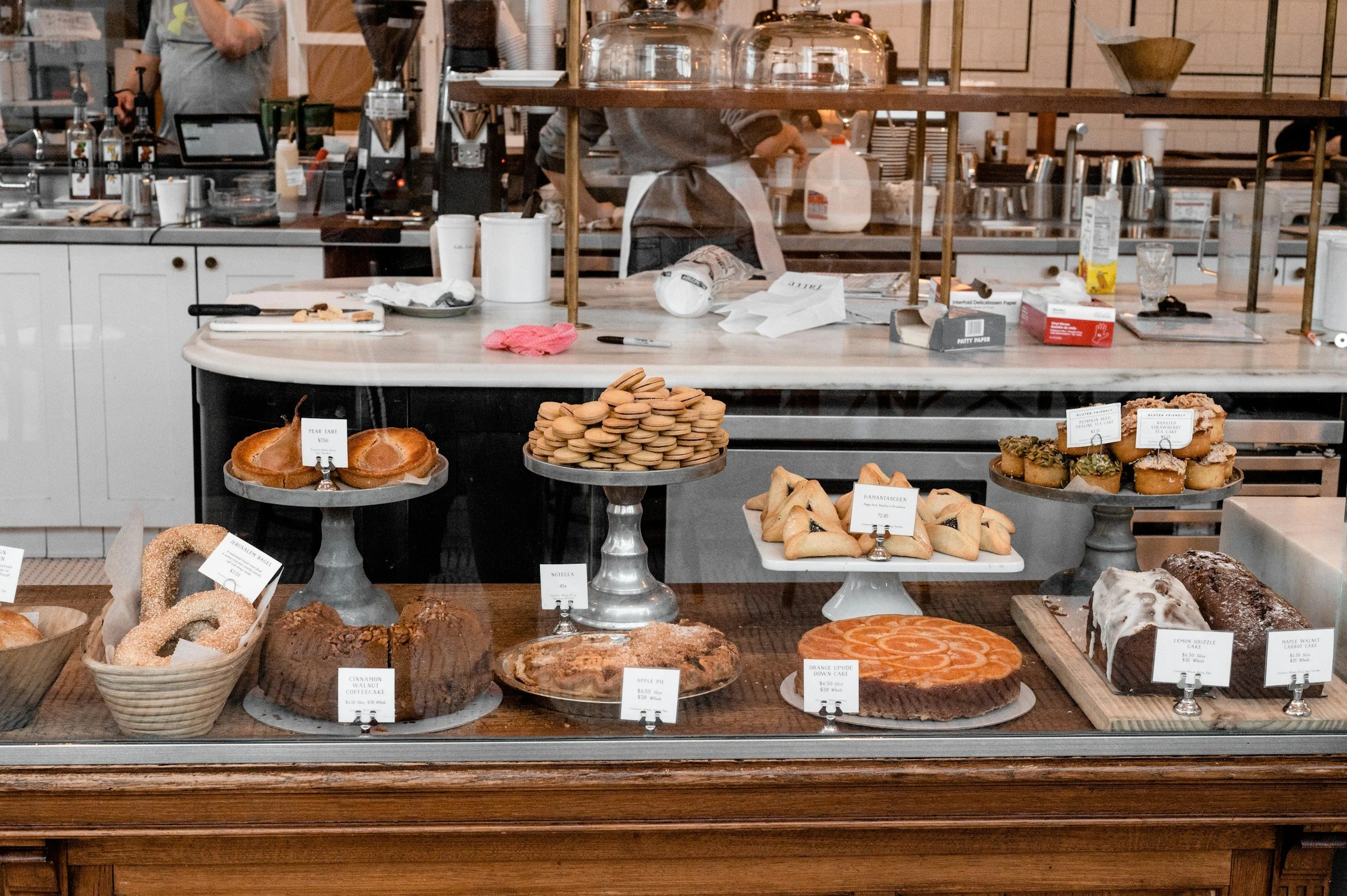 Display case with various baked goods including donuts, cookies, cakes, and pastries in a bakery or cafe setting.