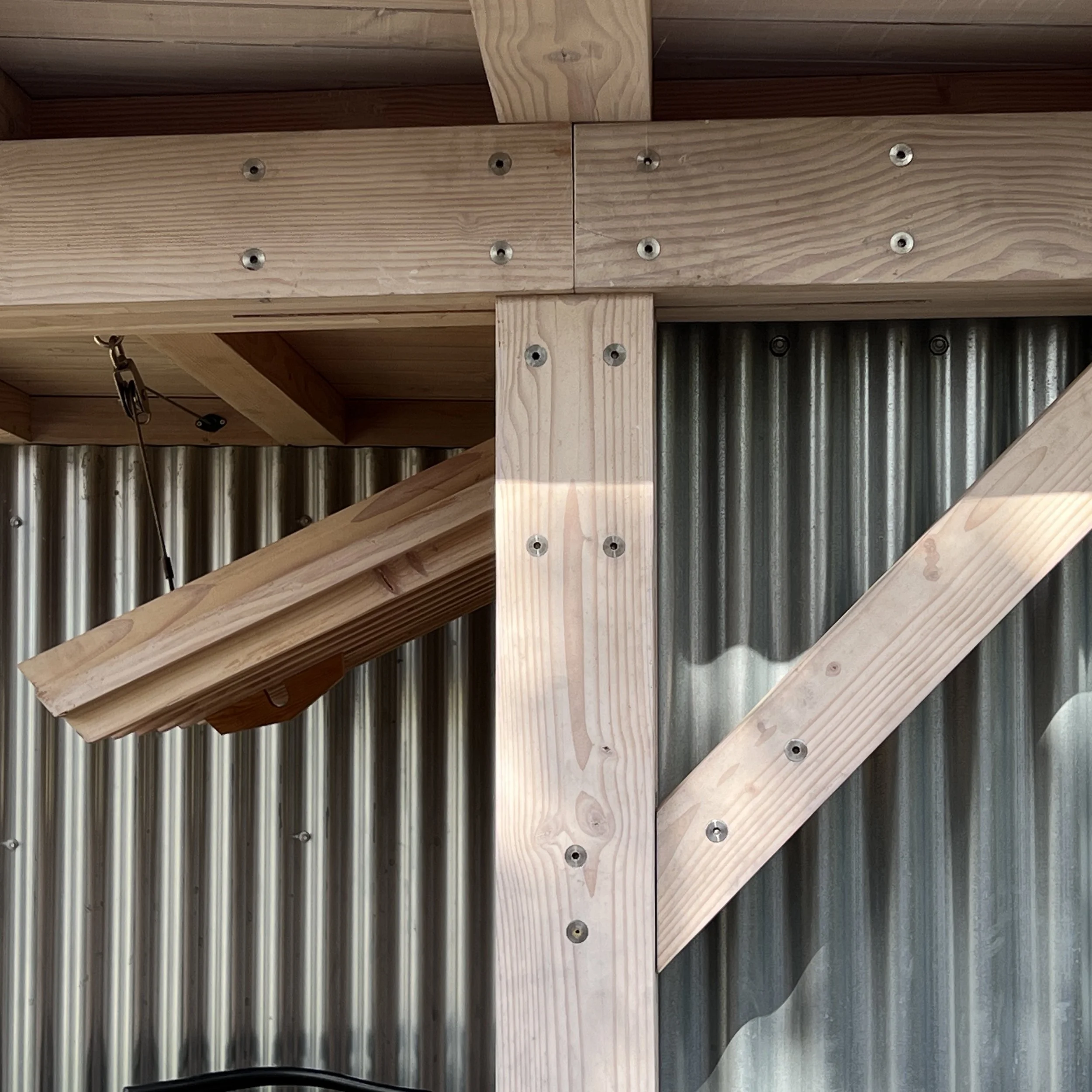 Contemporary architectural timber frame joint of douglas fir, stainless steel flitch plate and barrel nut fixings. Corrugated steel in background.